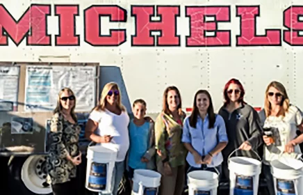 A group of women stand outside a Michels trailer holding buckets