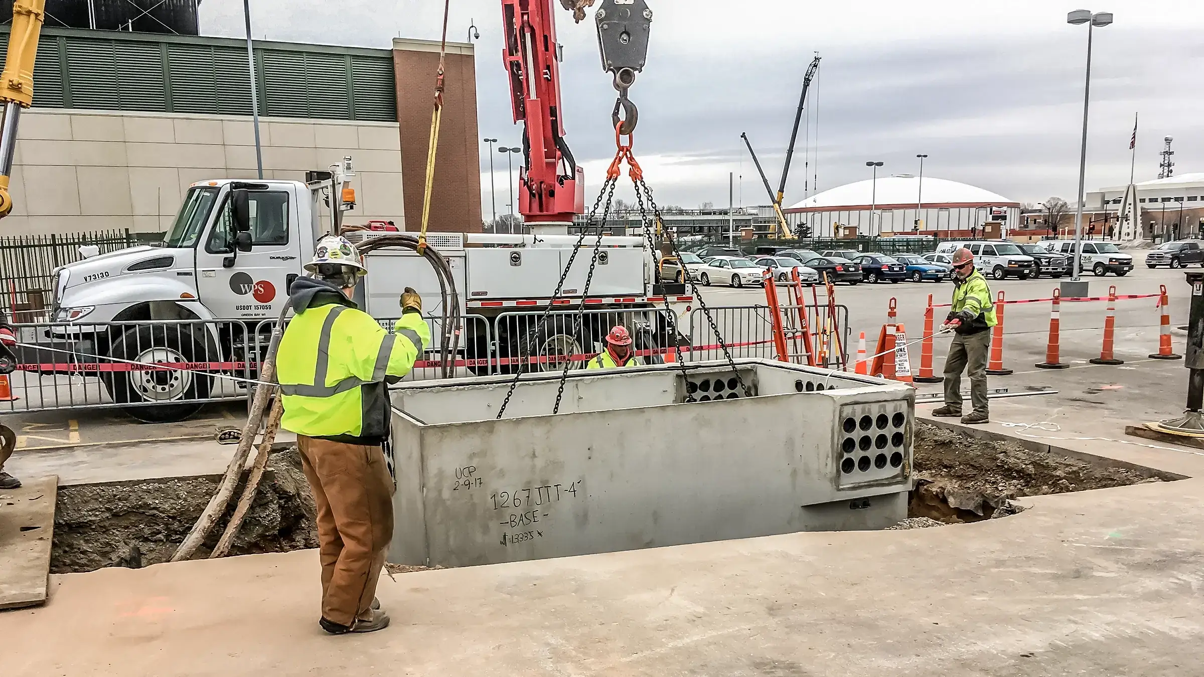 Three workers on a project in front of Lambeau field.