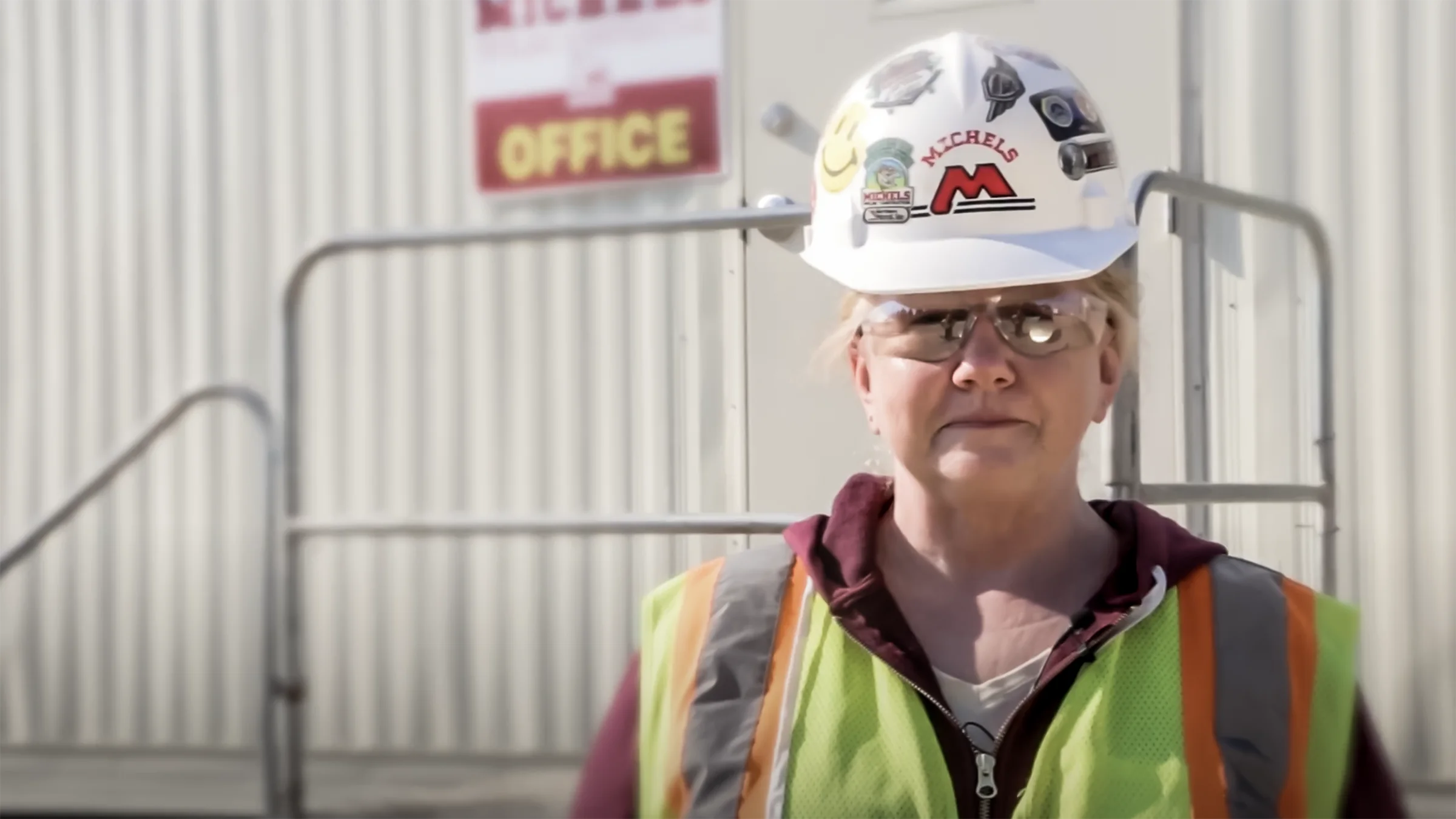 A woman wearing safety equipment stands near a field office