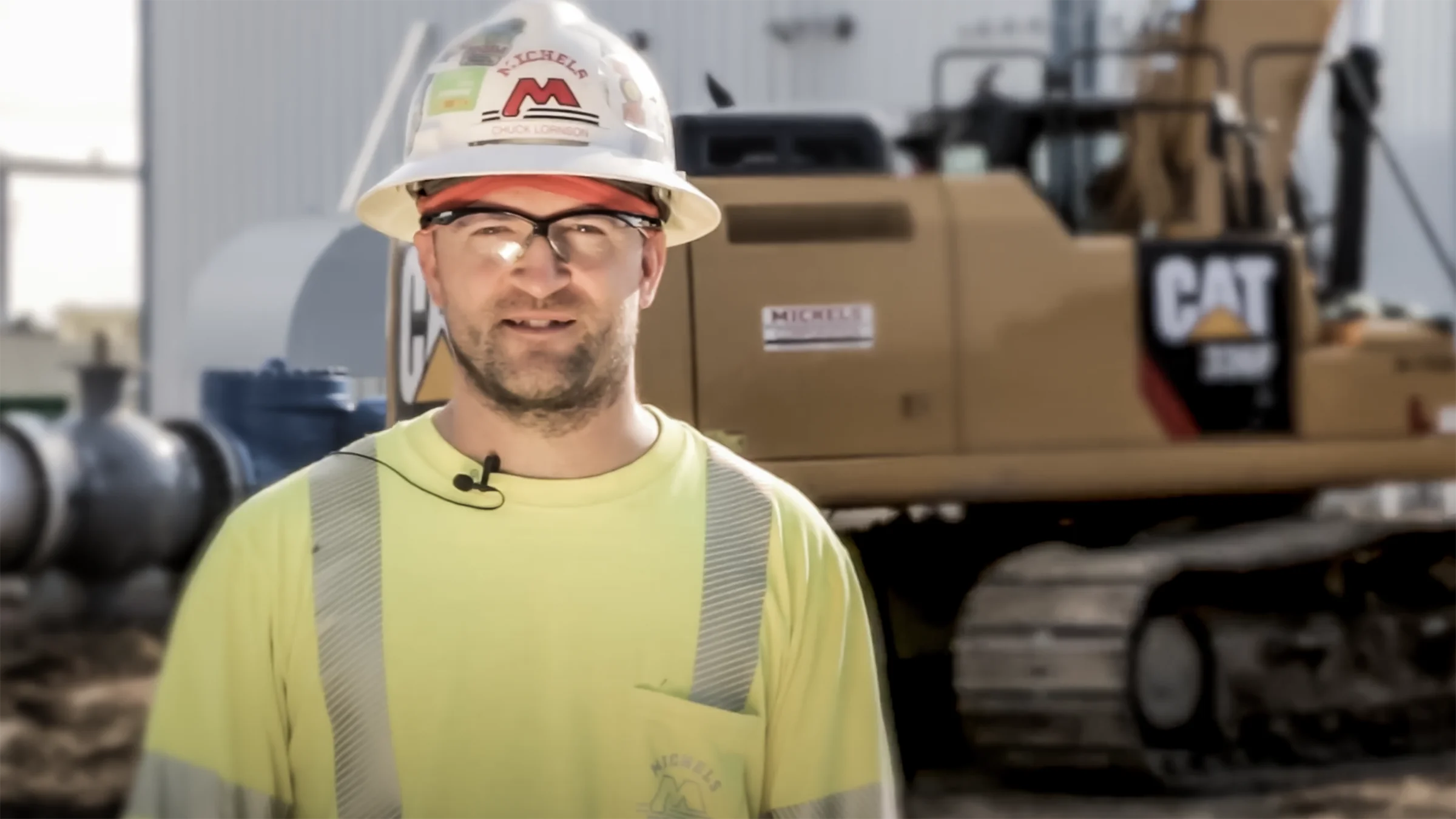 A man wearing safety equipment stands near an excavator