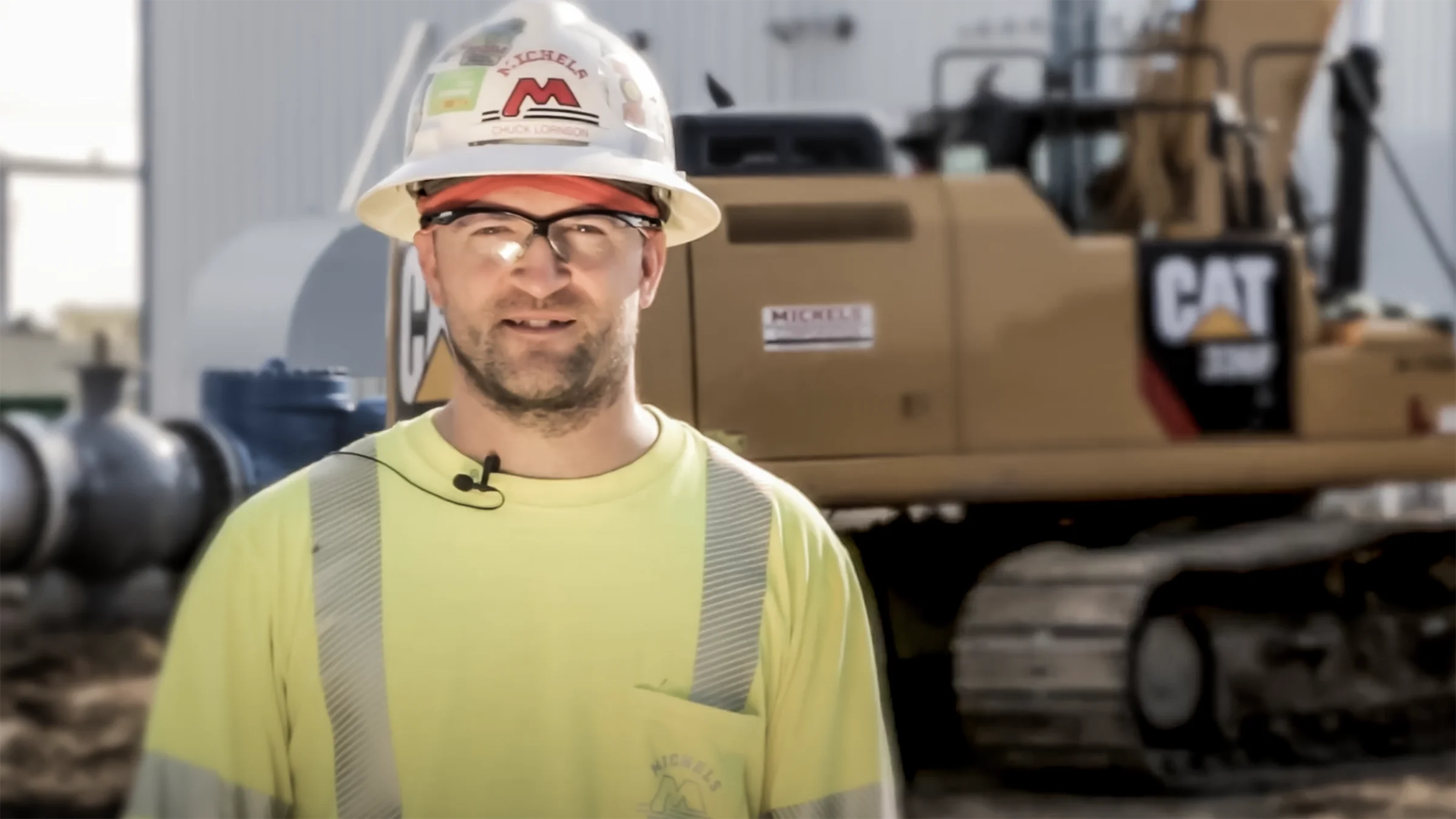 A man wearing safety estands near an excavator