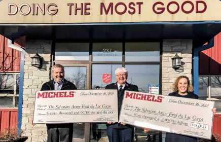 Michels stands outside of Salvation Army building with large checks