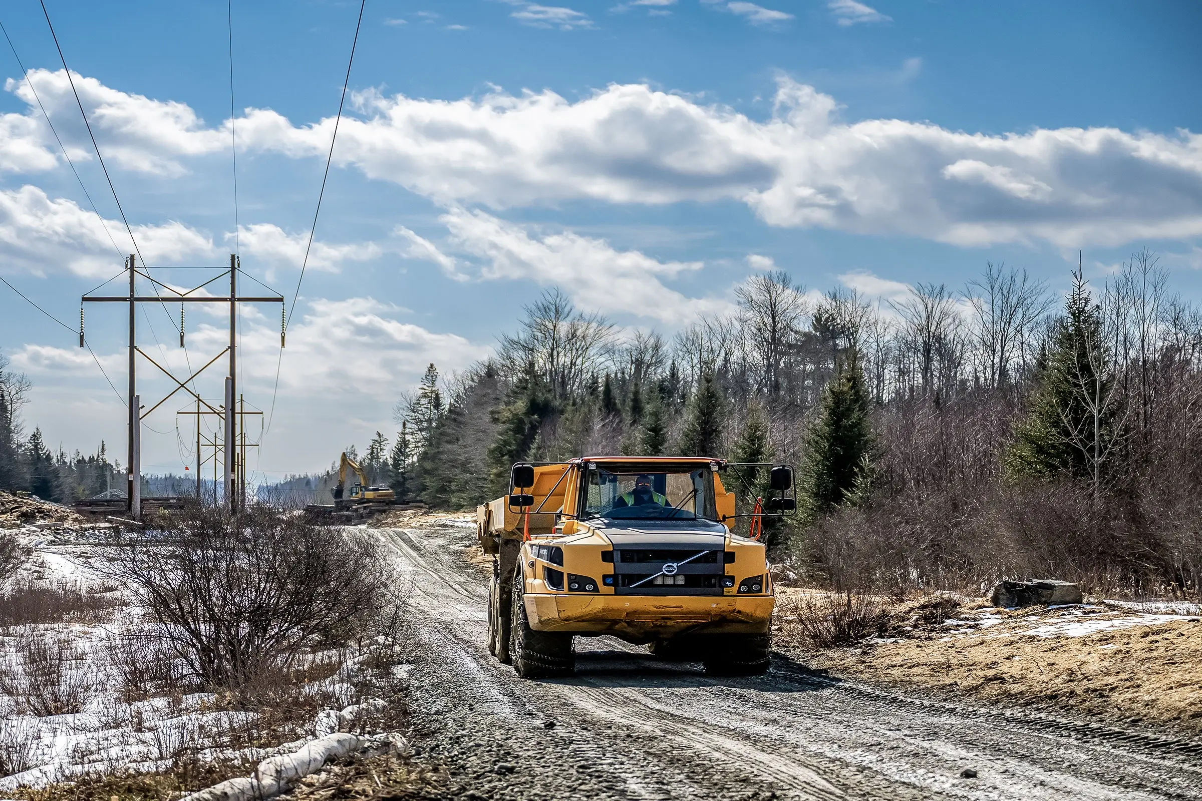 Heavy equipment traveling along dirt road on a partially sunny day.