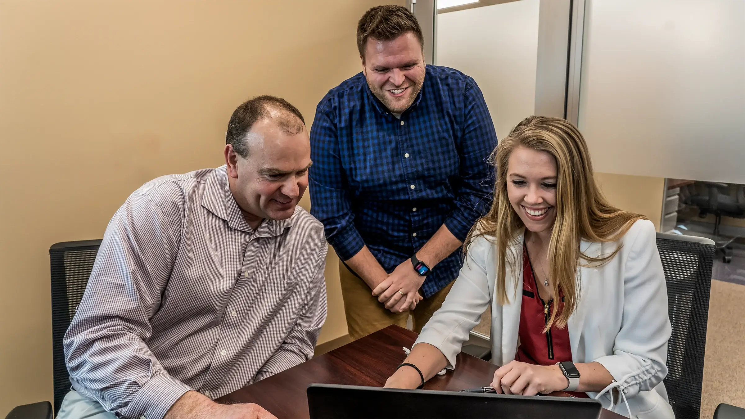 Three smiling people look at a computer screen