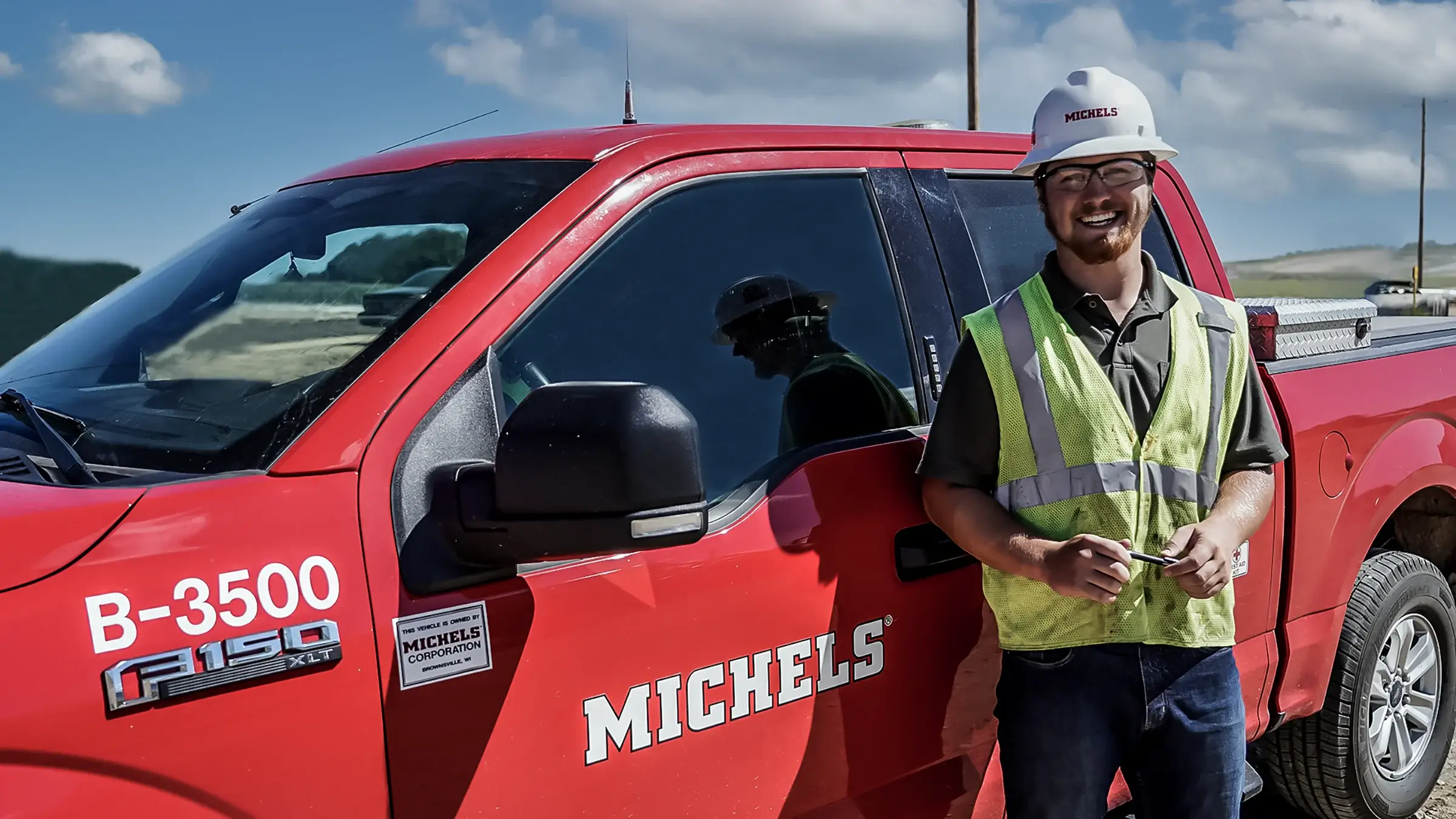 A smiling man stands next to a red pickup truck