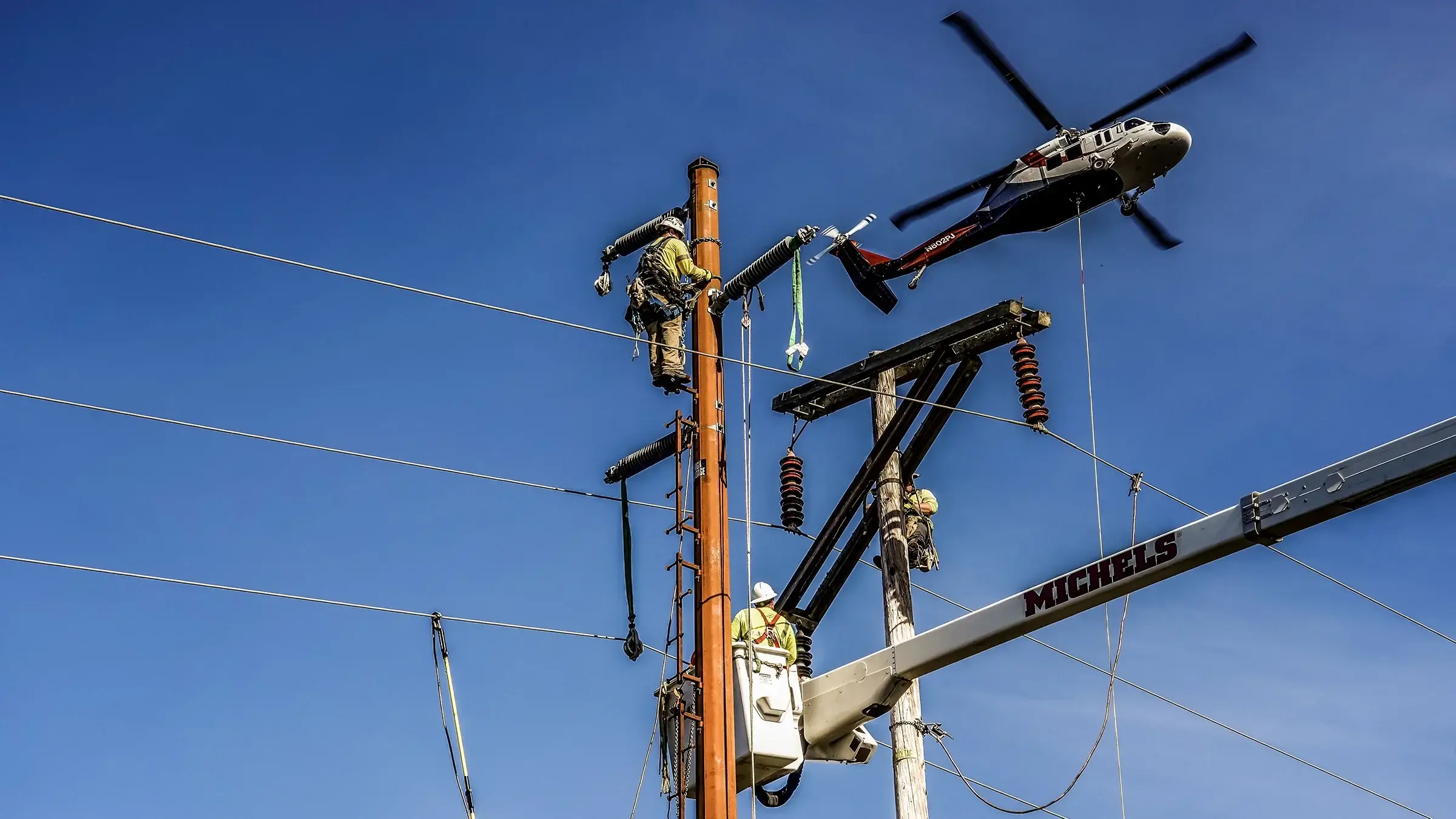 Power linemen work on power lines with support of a bucket truck and helicopter
