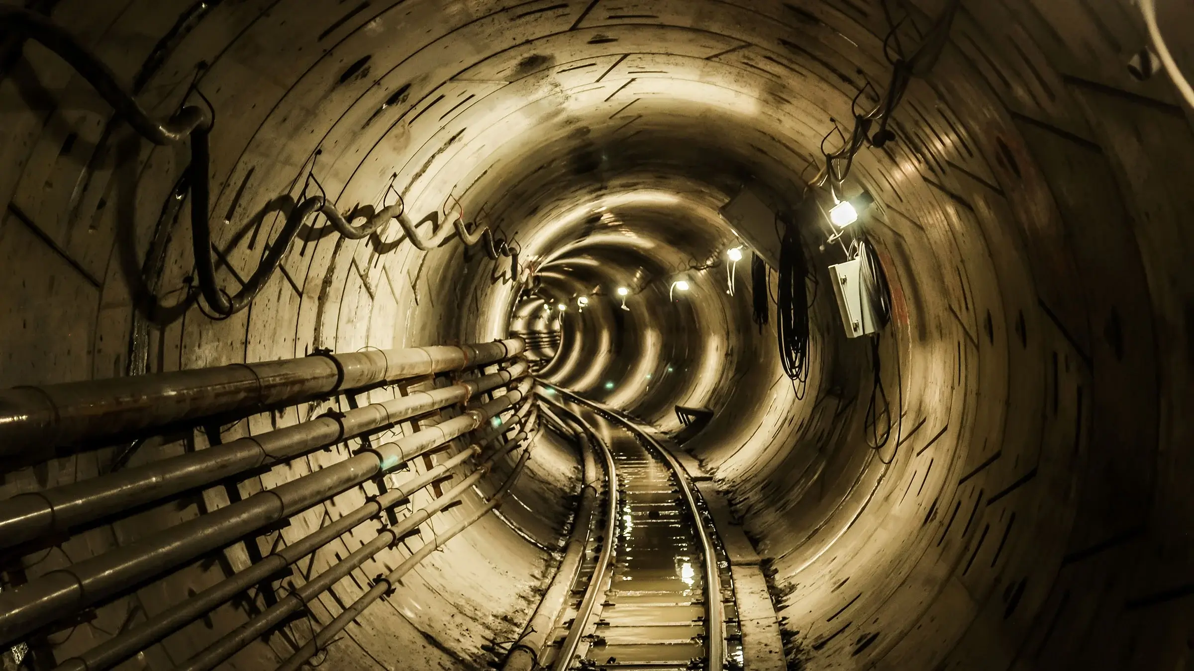 Sewer pipes running along a lighted underground tunnel