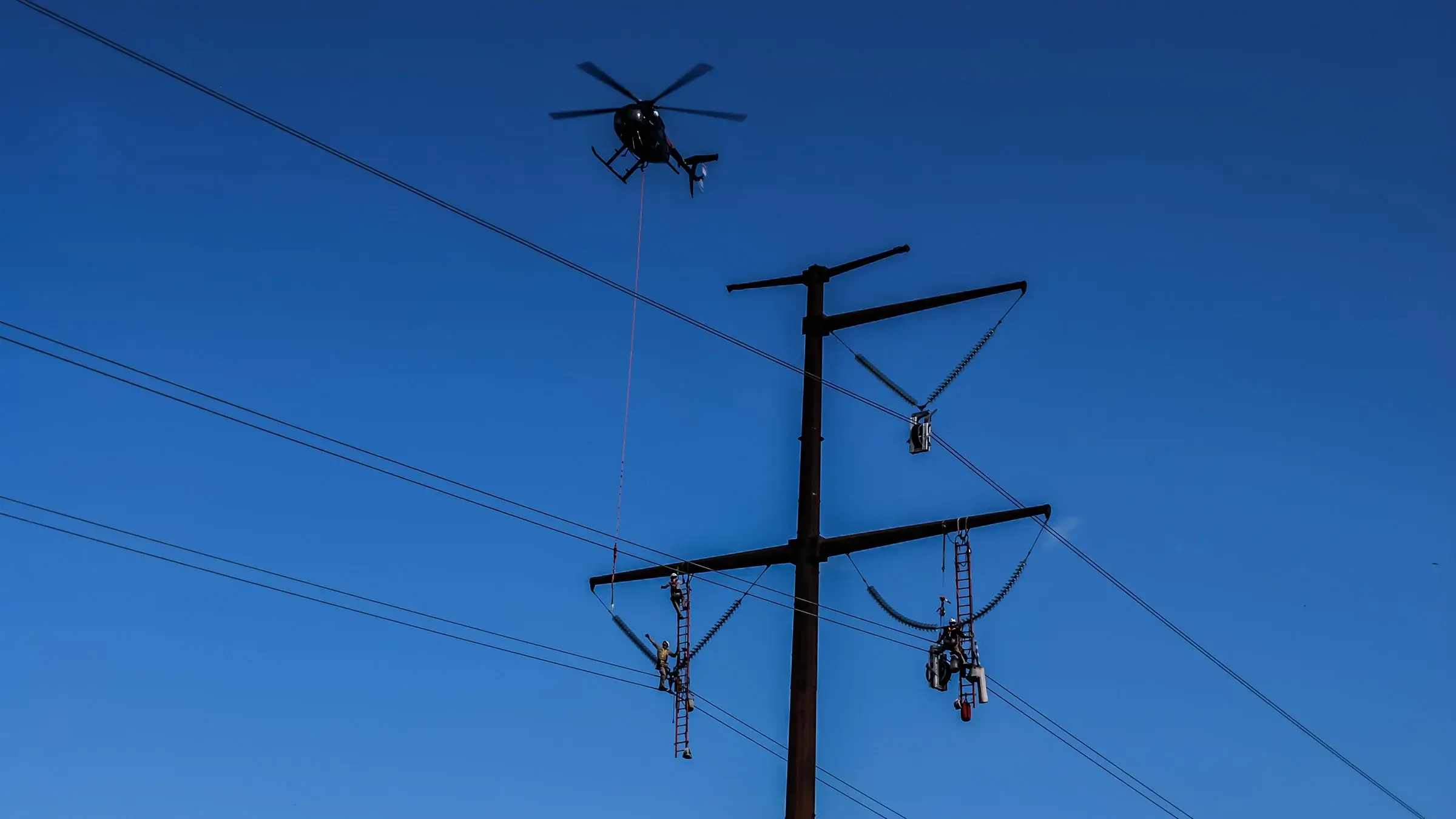 Helicopter flies over crew on power poles to provide them with more equipment