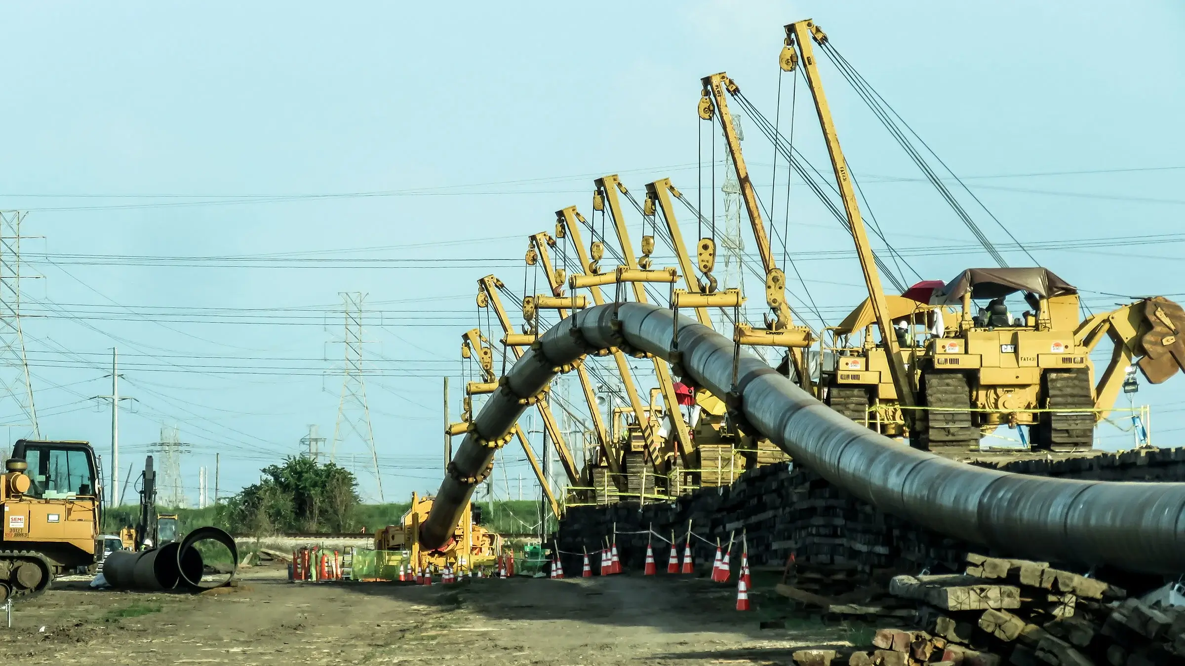 A group of pipe-layer machines hoist a large pipeline in the air leading to a Direct Pipe rig.