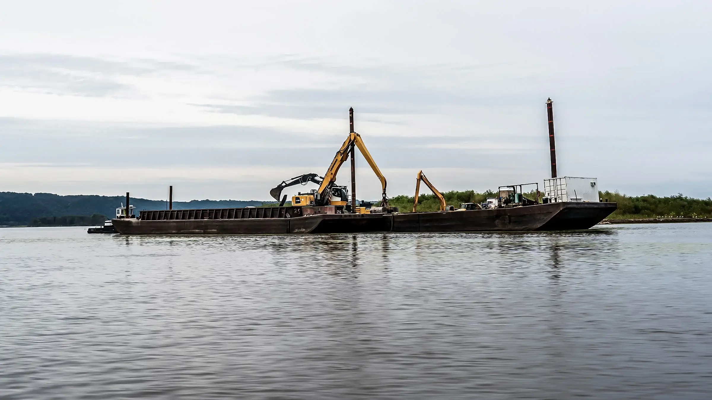 Excavators transfer materials from one barge to another on a lake