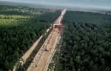A large scale pipeline project spans across a densely forested area.