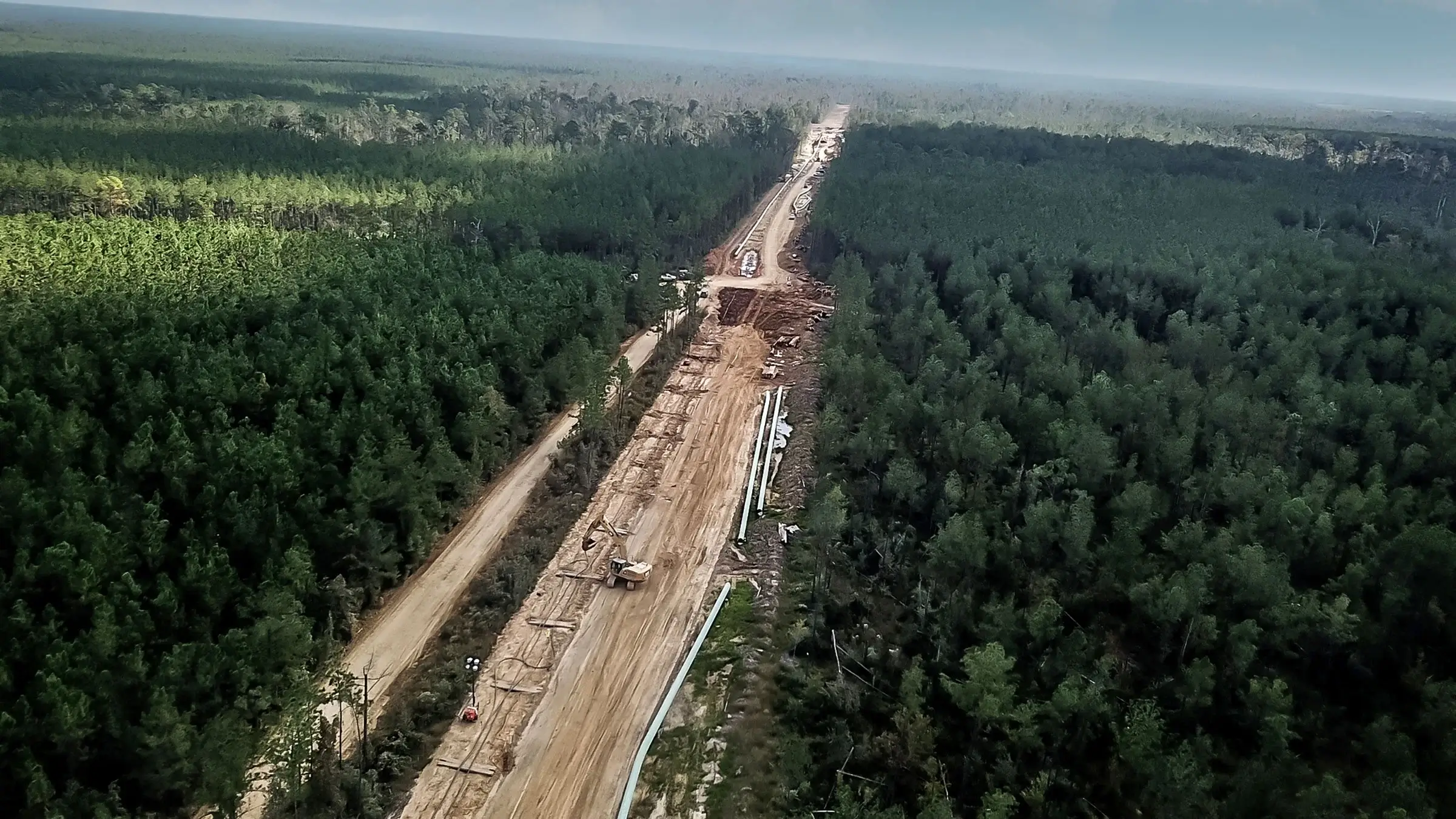 A large scale pipeline project spans across a densely forested area.