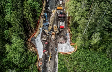 Multiple cranes and other large equipment work on a foundations project in a forest
