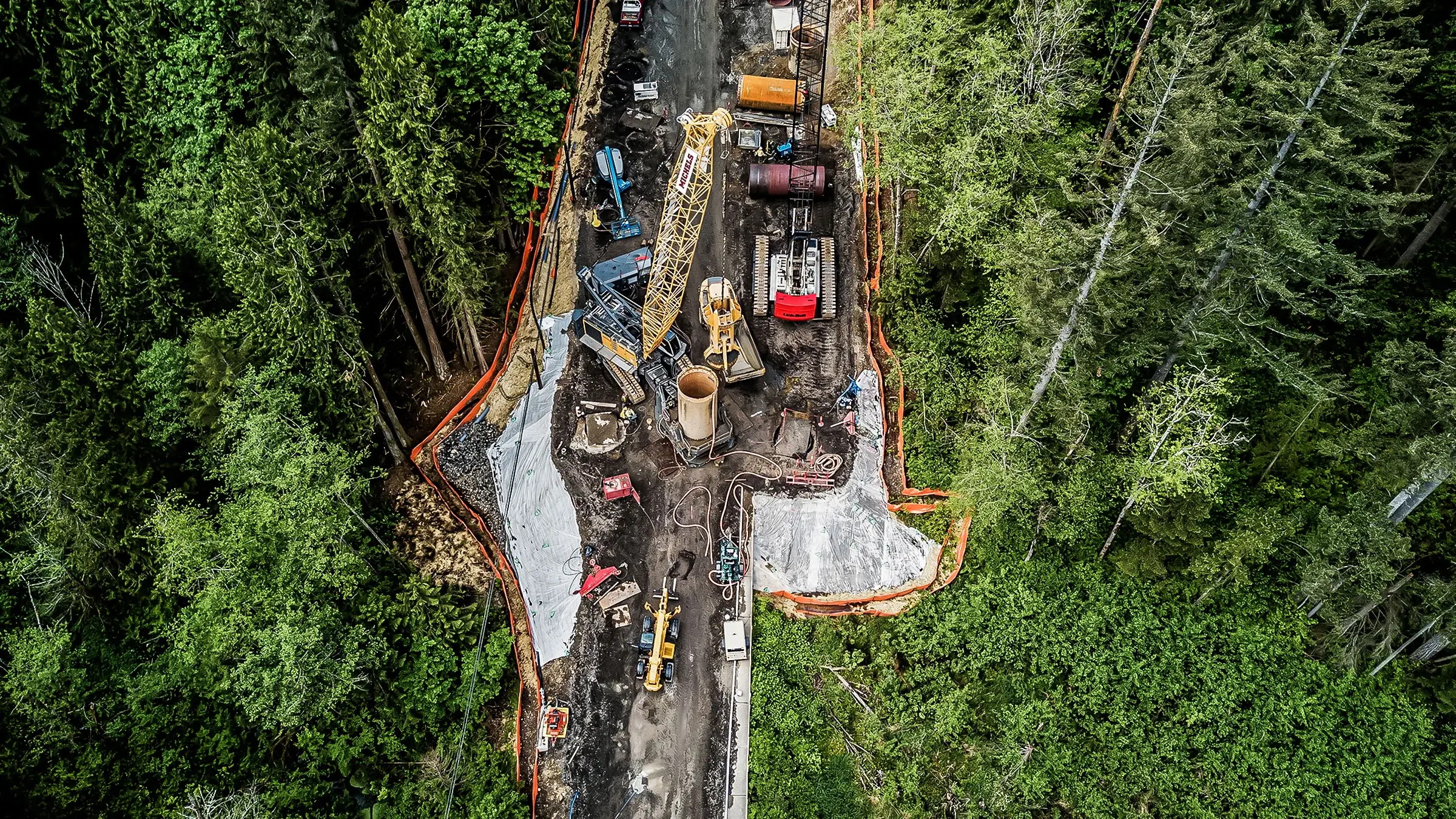 Multiple cranes and other large equipment work on a foundations project in a forest
