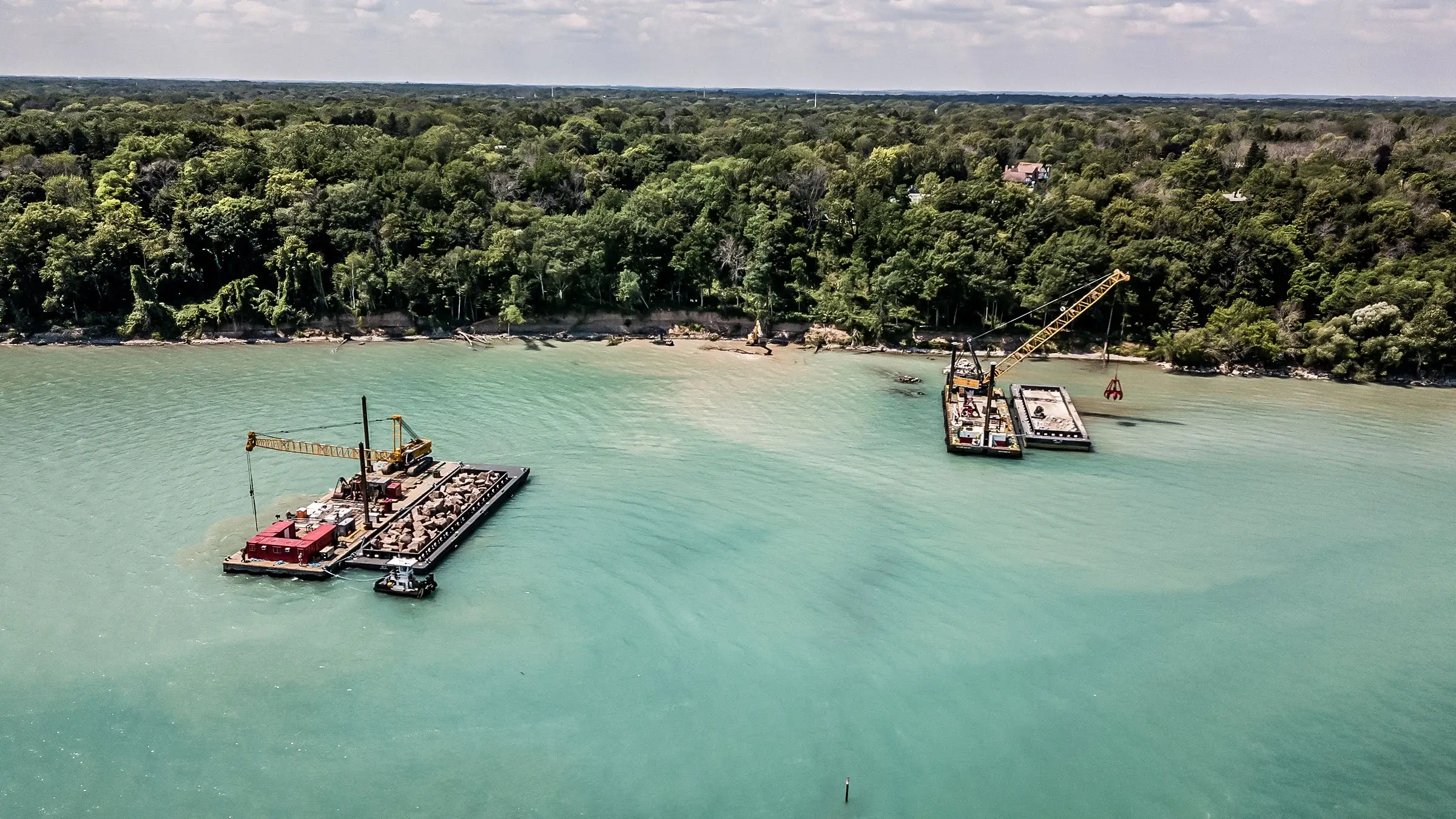 Two barges with cranes operate off-shore near the Lake Michigan coast line