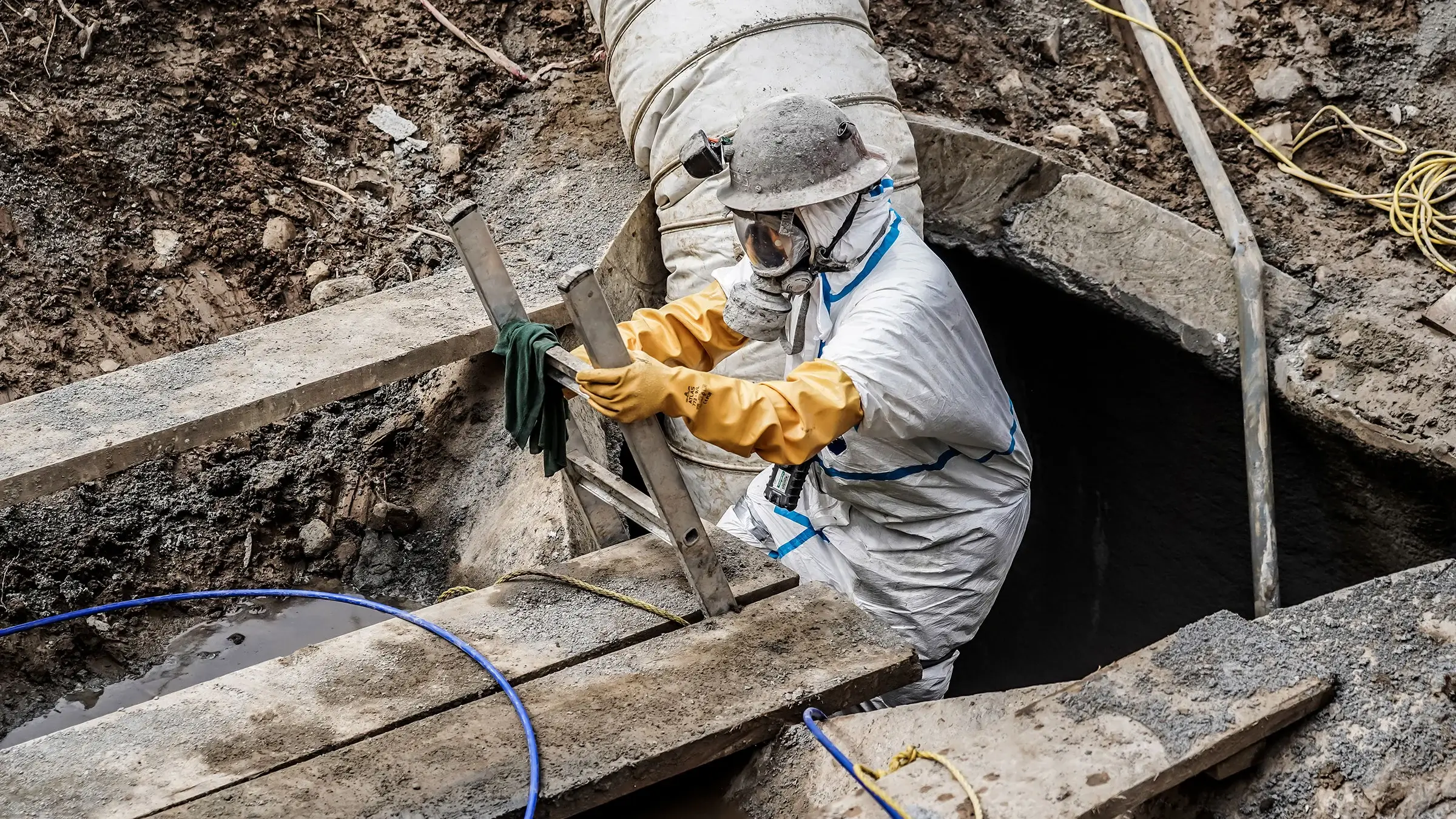 Crew member climbs out of pipe wearing PPE for spraying geopolymer mortar to rehab sewer pipe
