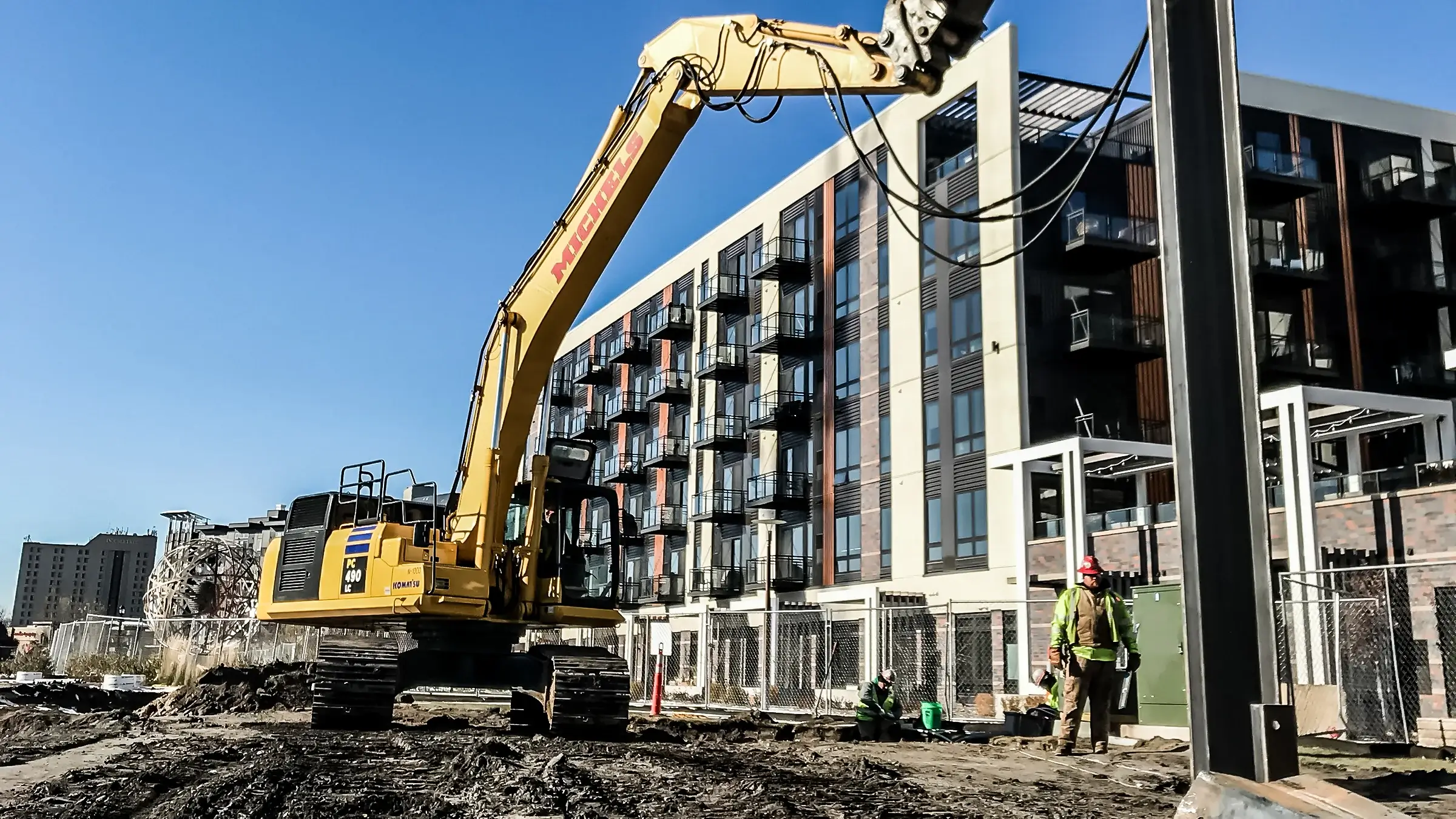 An excavator operates on a foundations job near an housing complex.
