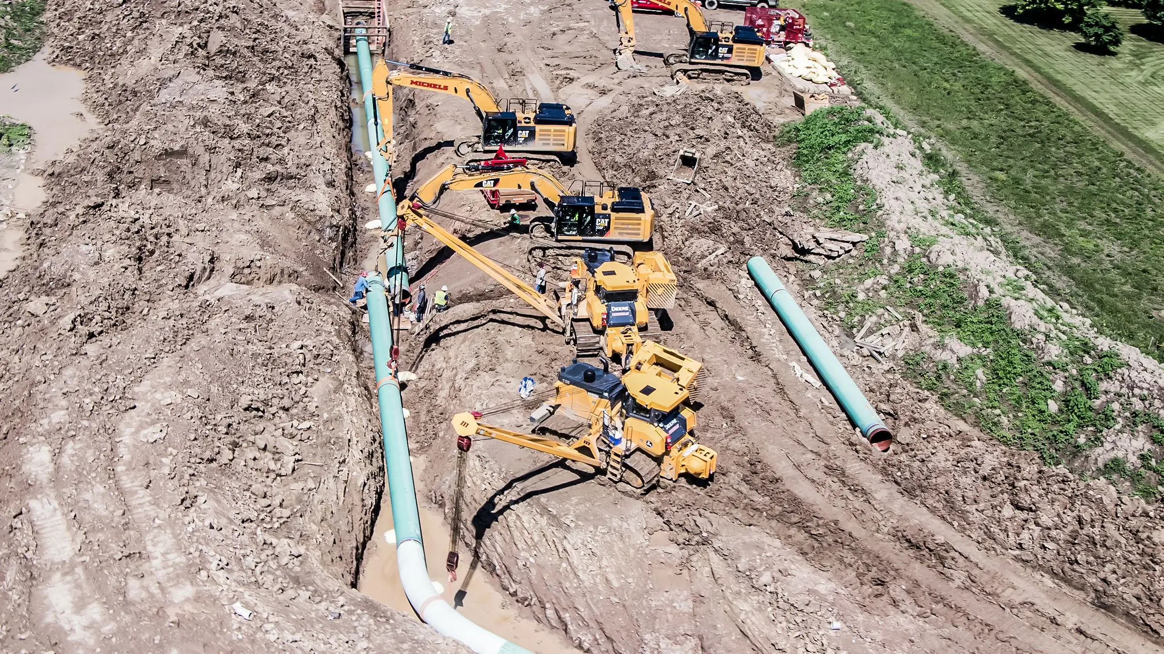 Sidebooms and excavators adjust pipeline after placing in curved trench