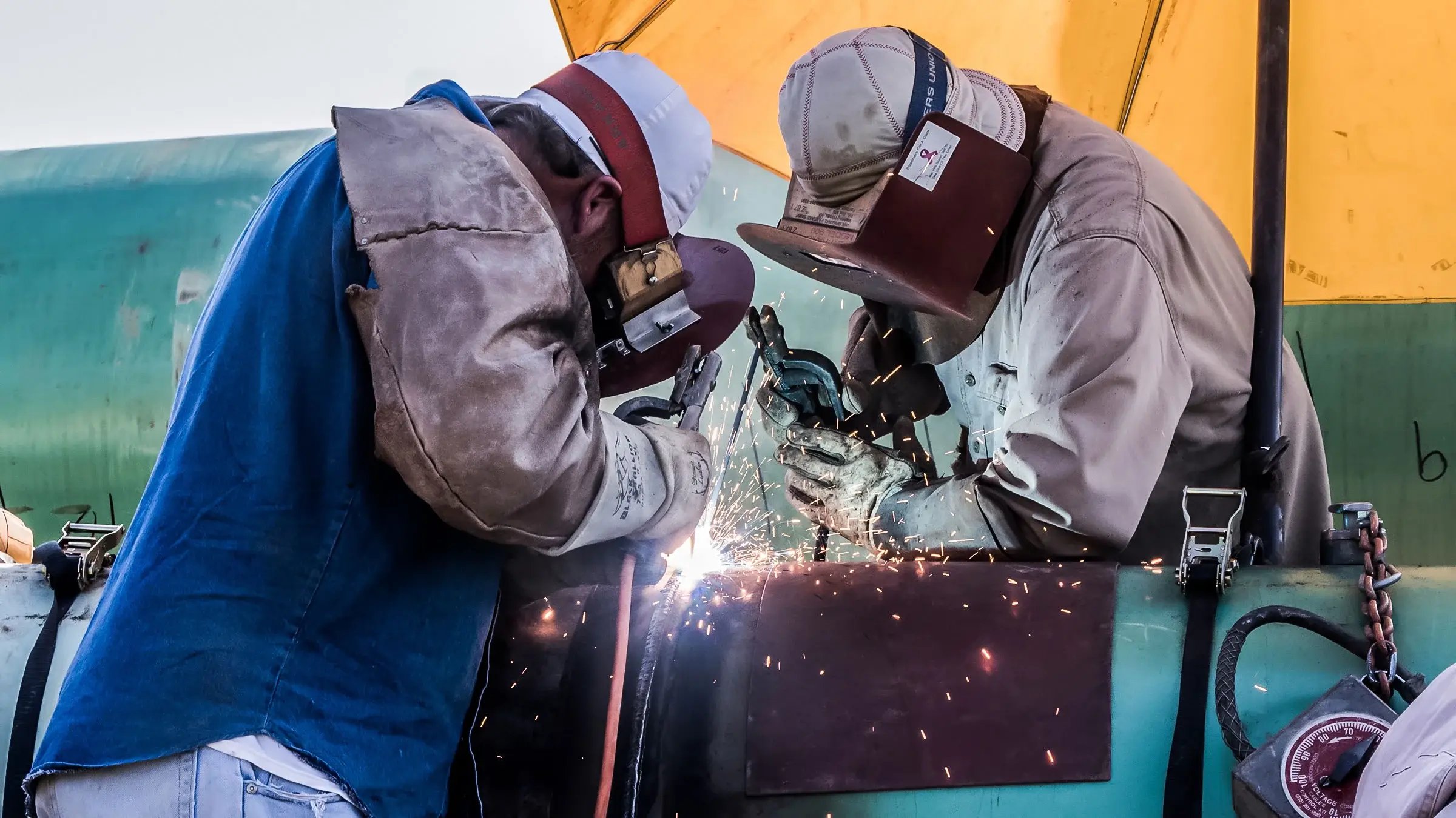 Two welders working on section of pipeline with sparks flying