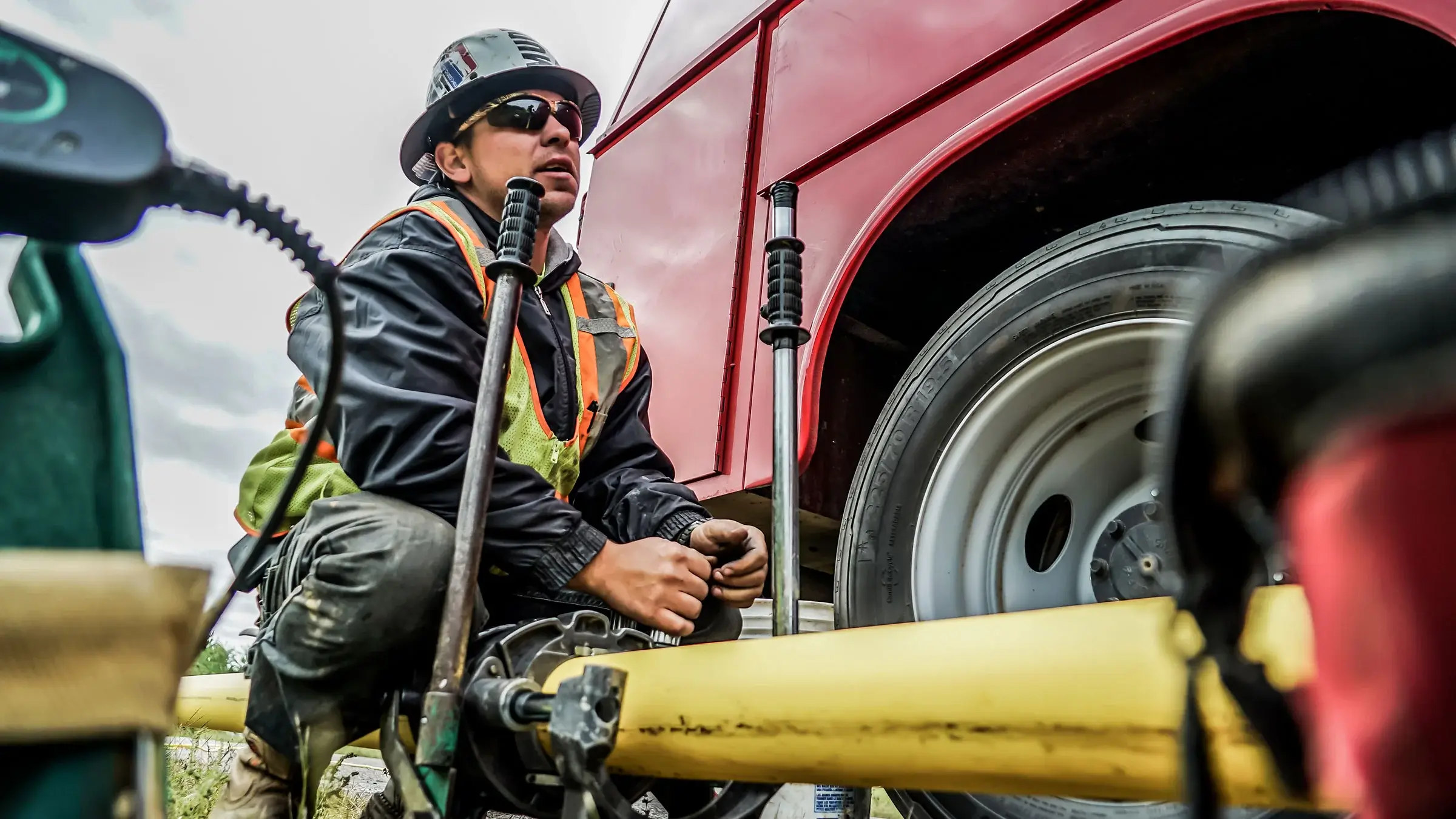 A crew member observes and inspects a small pipe near a truck