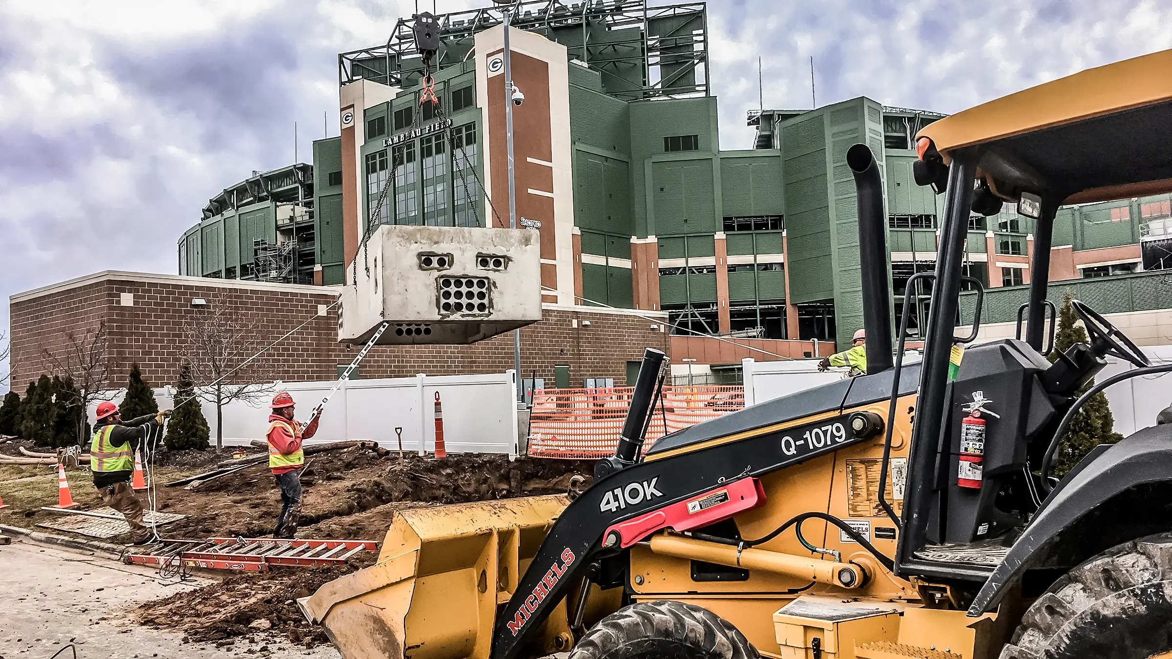 Two workers on a project in front of Lambeau field.