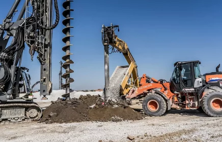 A drill rig, backhoe, and excavator all work at the same spot on a foundation