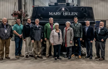 The Michels family and executives stand in front of the Mary Helen tugboat.