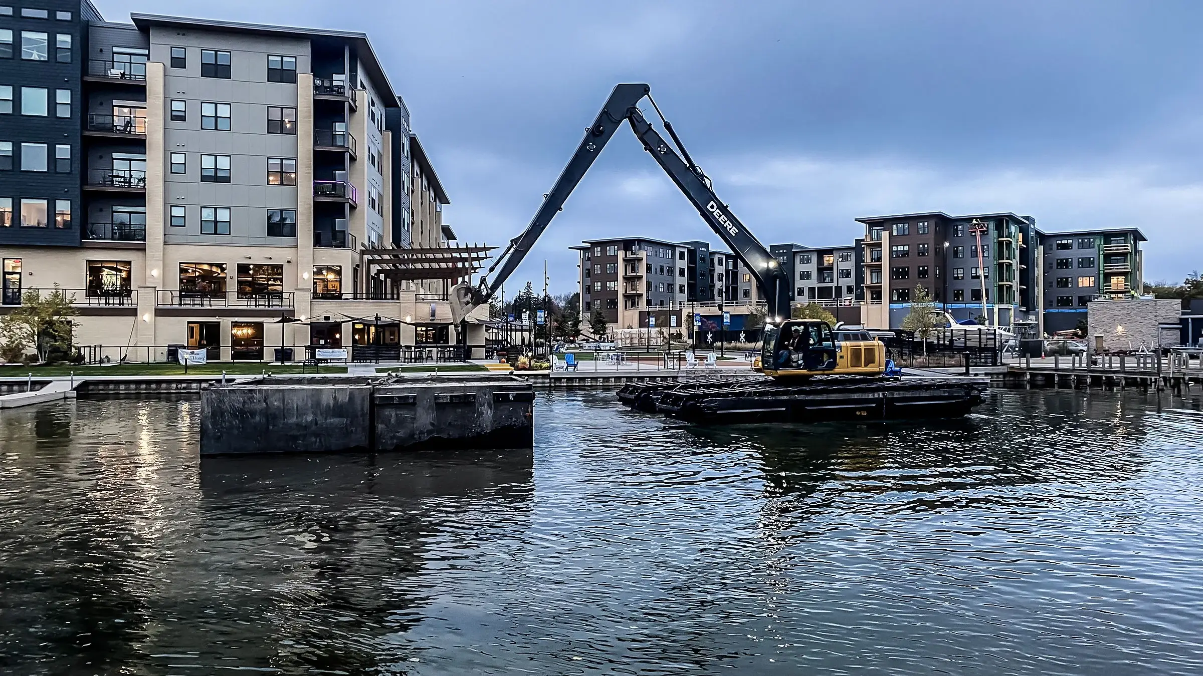 An amphibious excavator operates in a channel near condo homes