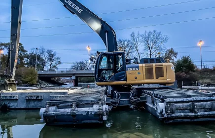 An amphibious excavator loads a container with dregding material