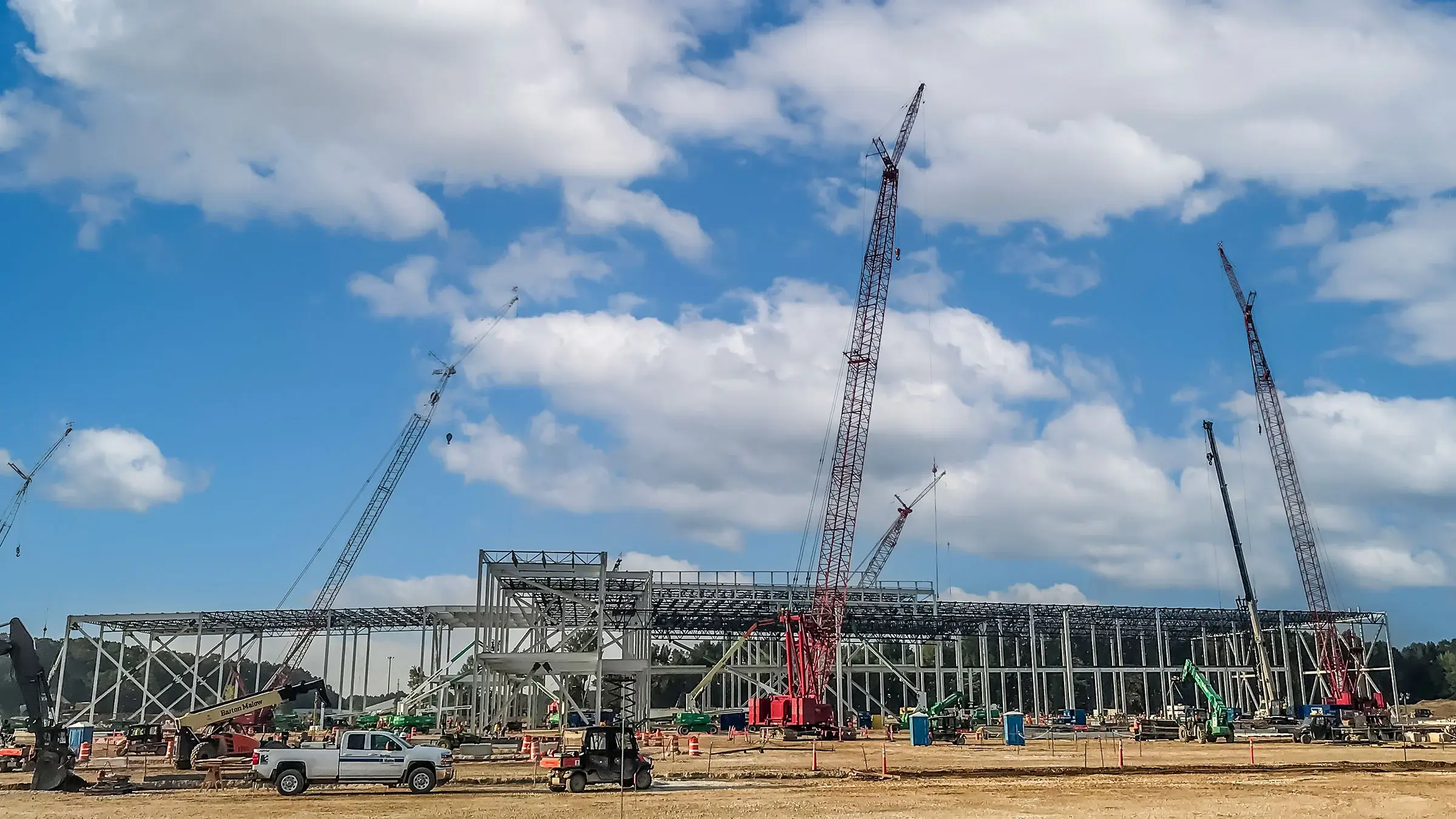 Large cranes and drilling equipment work on constructing a large battery facility plant.