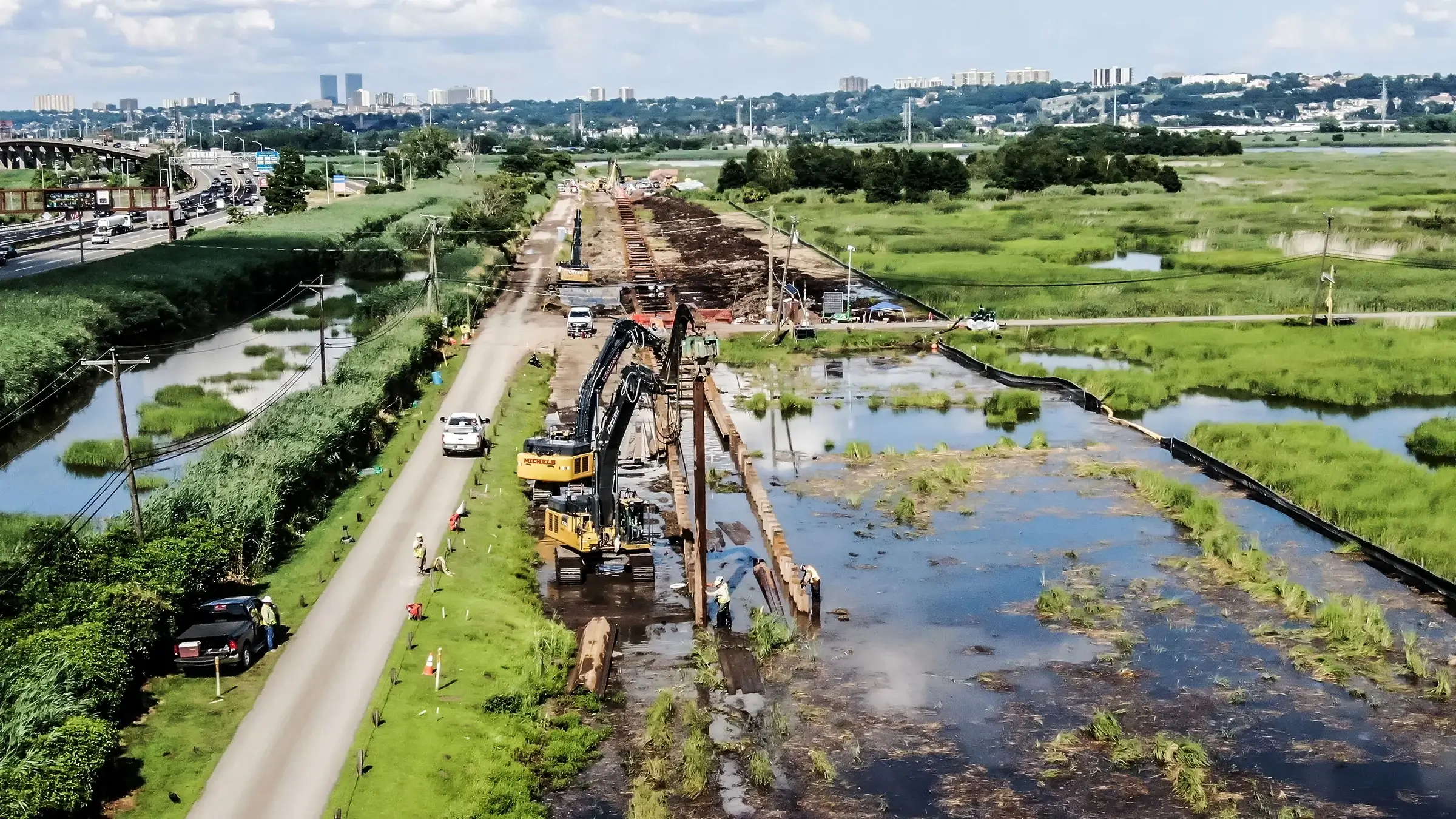 Large excavators work near a road and marsh