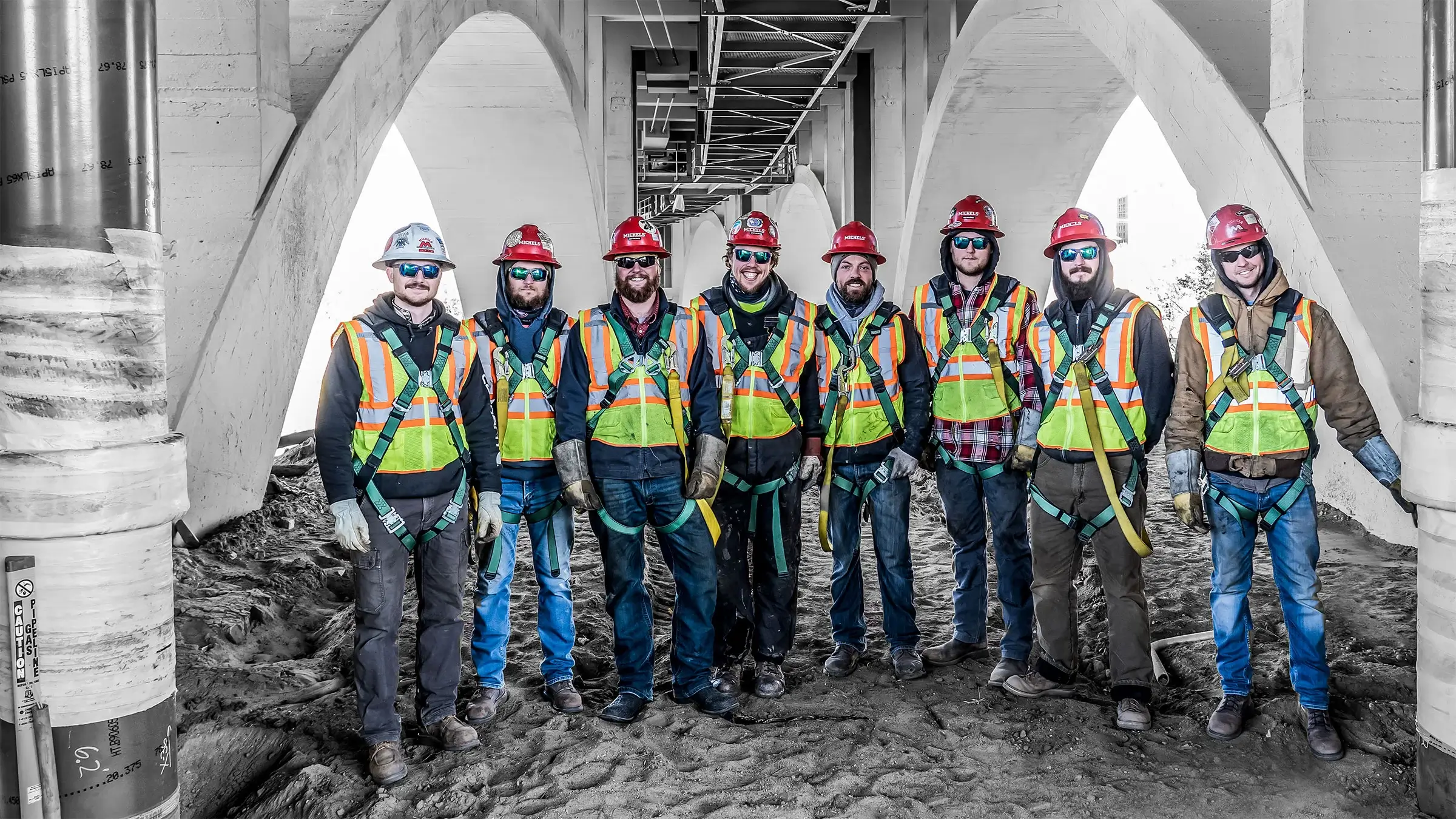 A group of Michels Utility Services workers stand together underneath a bridge overpass.