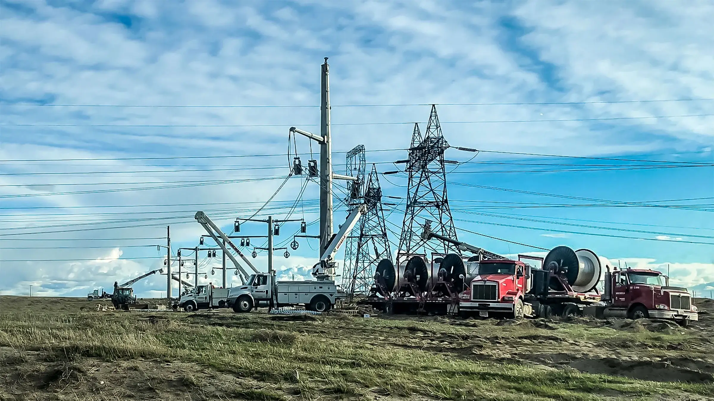 Electrical line workers connect power lines to a tower against a blue sky