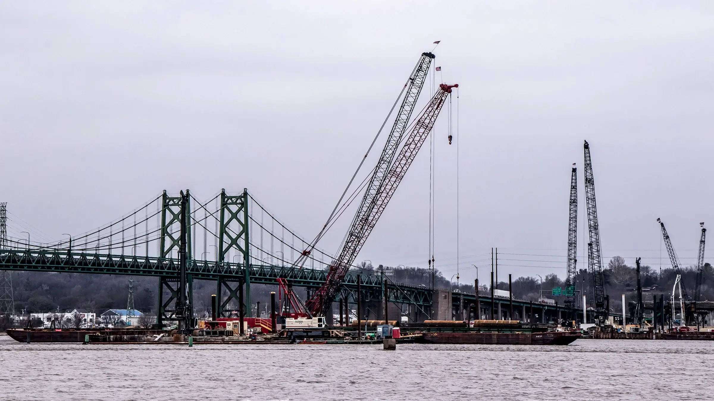 Cranes performing work on large bridge over a river.