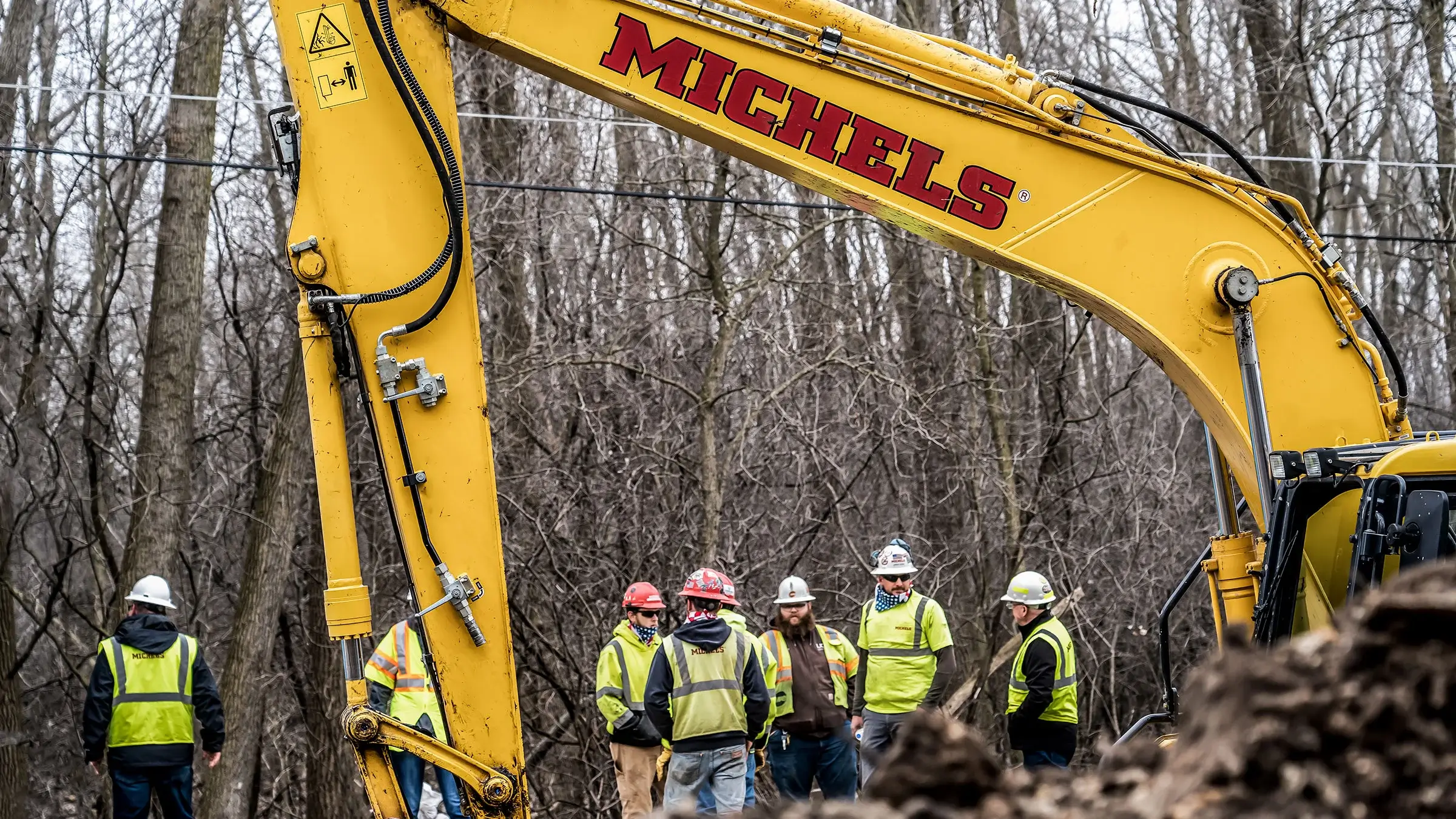 A Michels crew stands outside near an excavator.