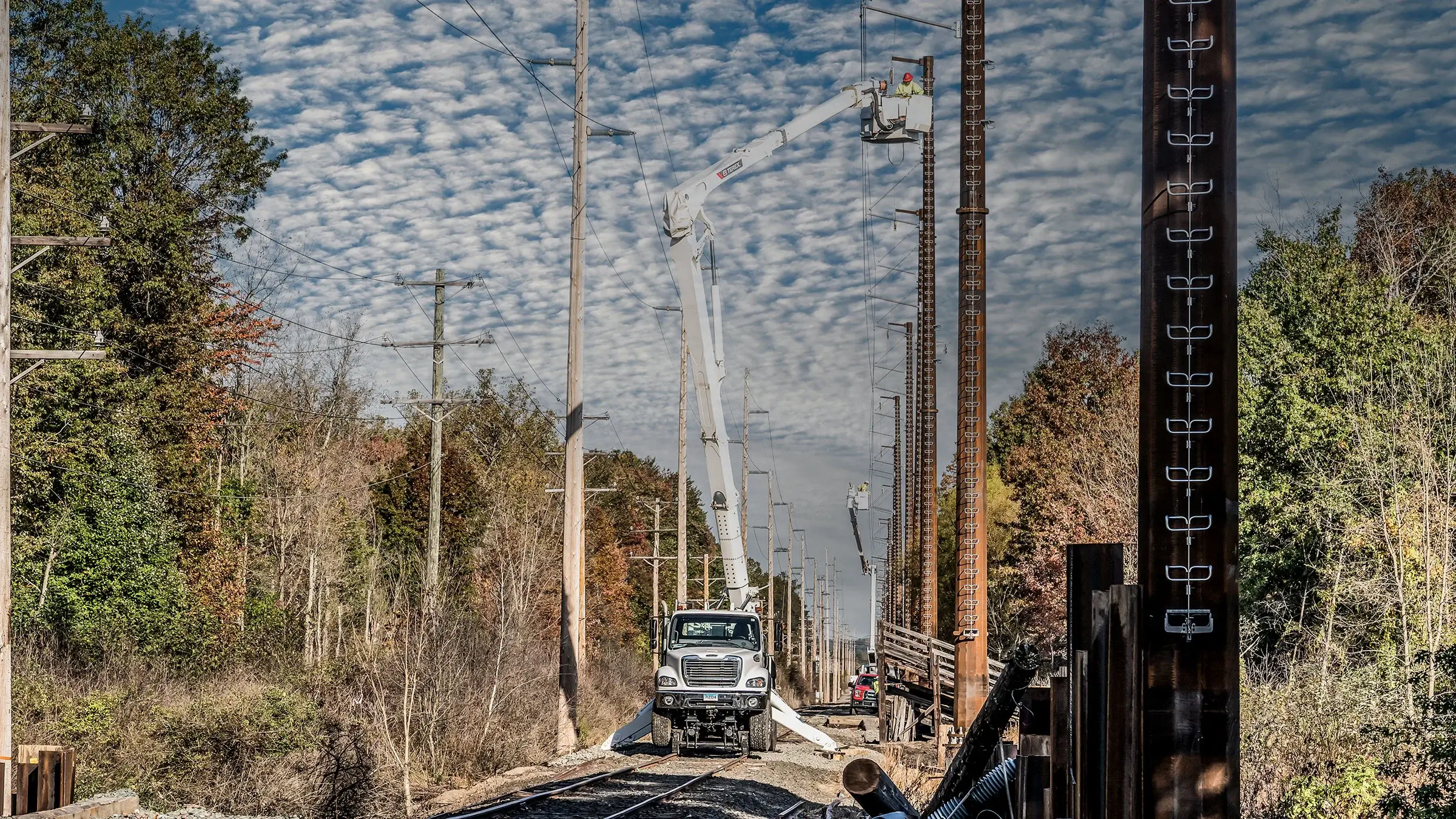 A crew works on hi-rail equipment to build a power line next to railroad tracks