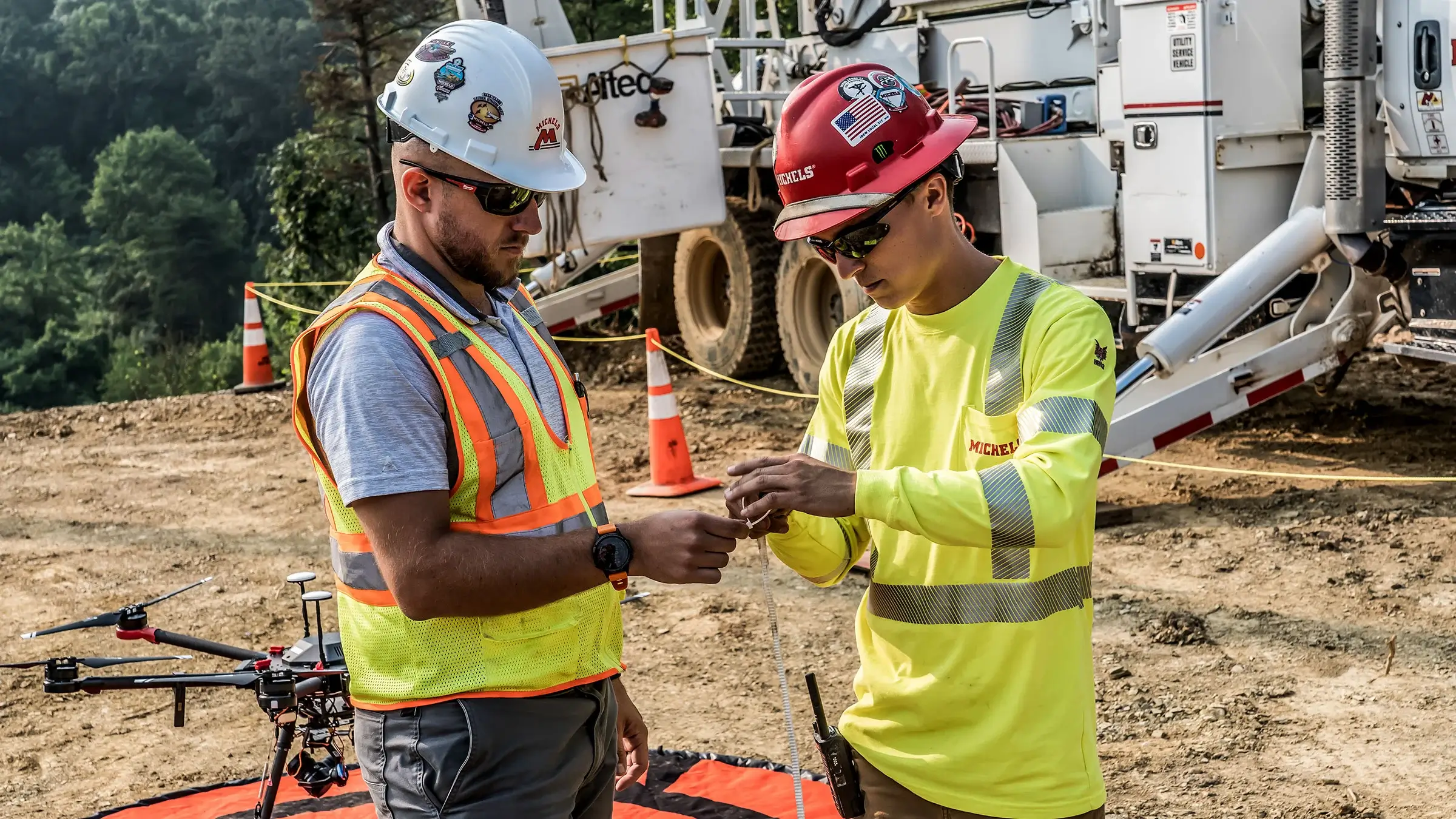 Two interns work on a wire with a large drone behind them.