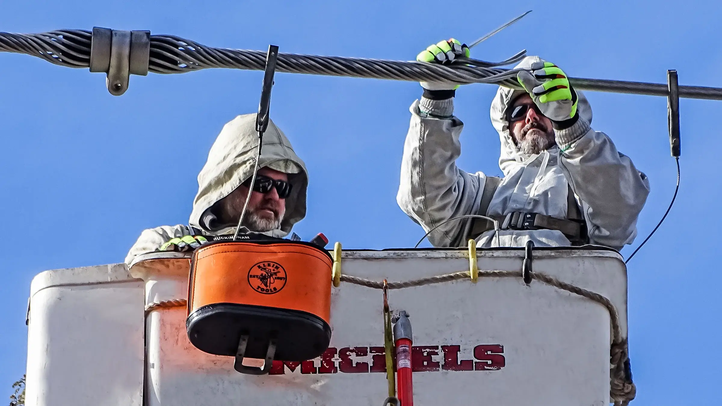Two Michels linemen work on a power line from a bucket truck.