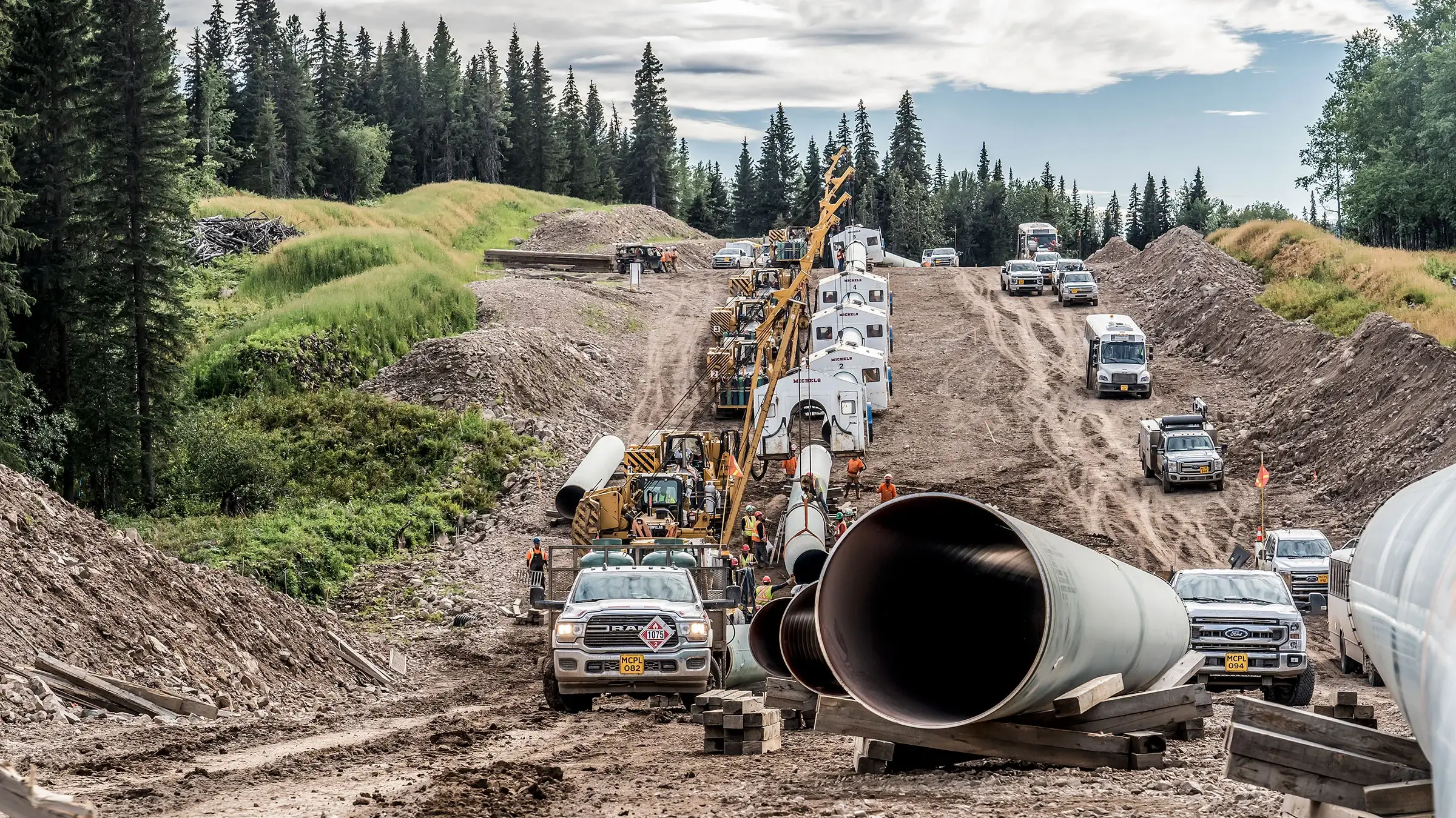 Michels Canada workers operate along a large pipeline in a forested area.