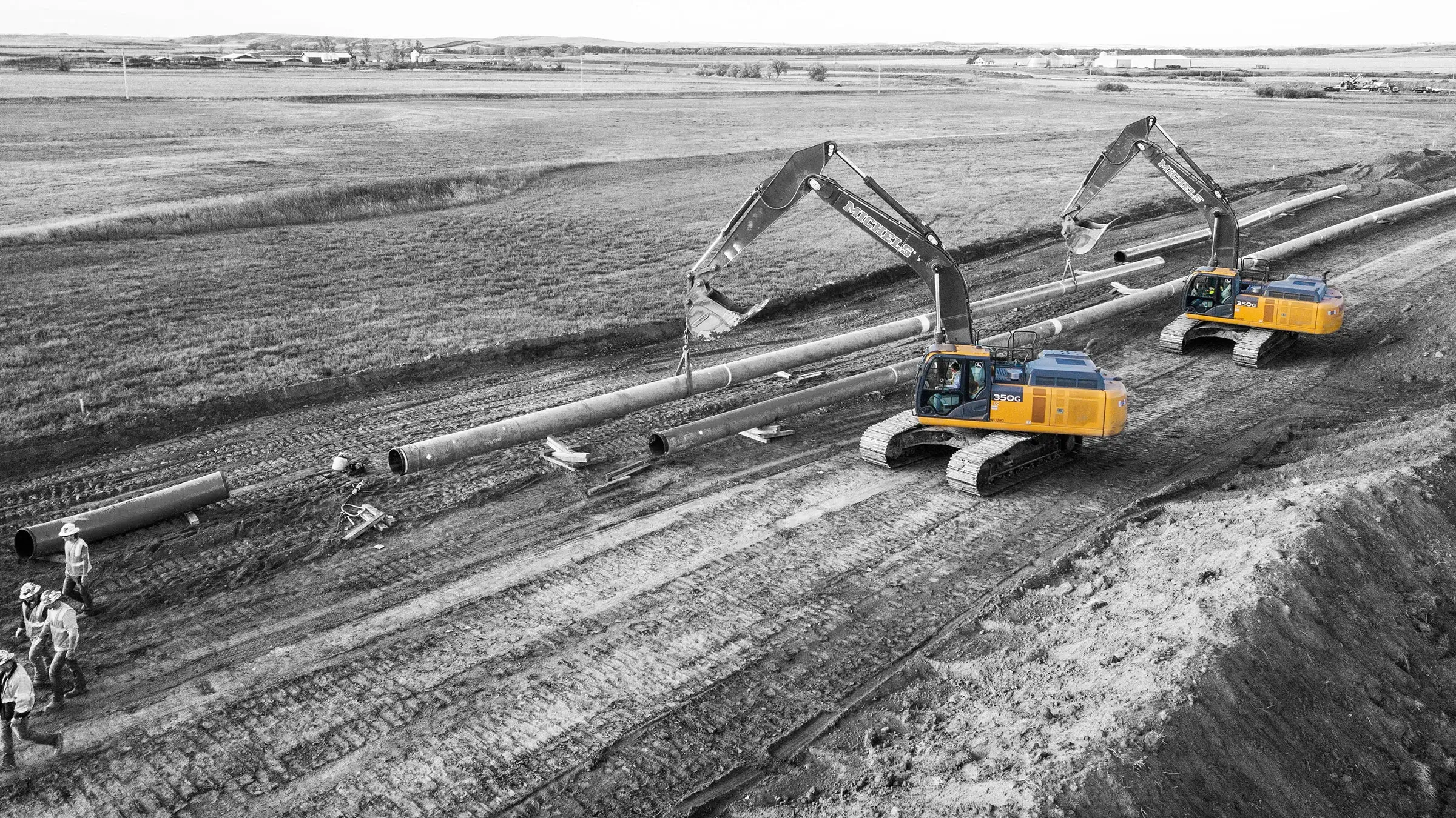 Two excavators assist in supporting the weight of a segment of pipe.