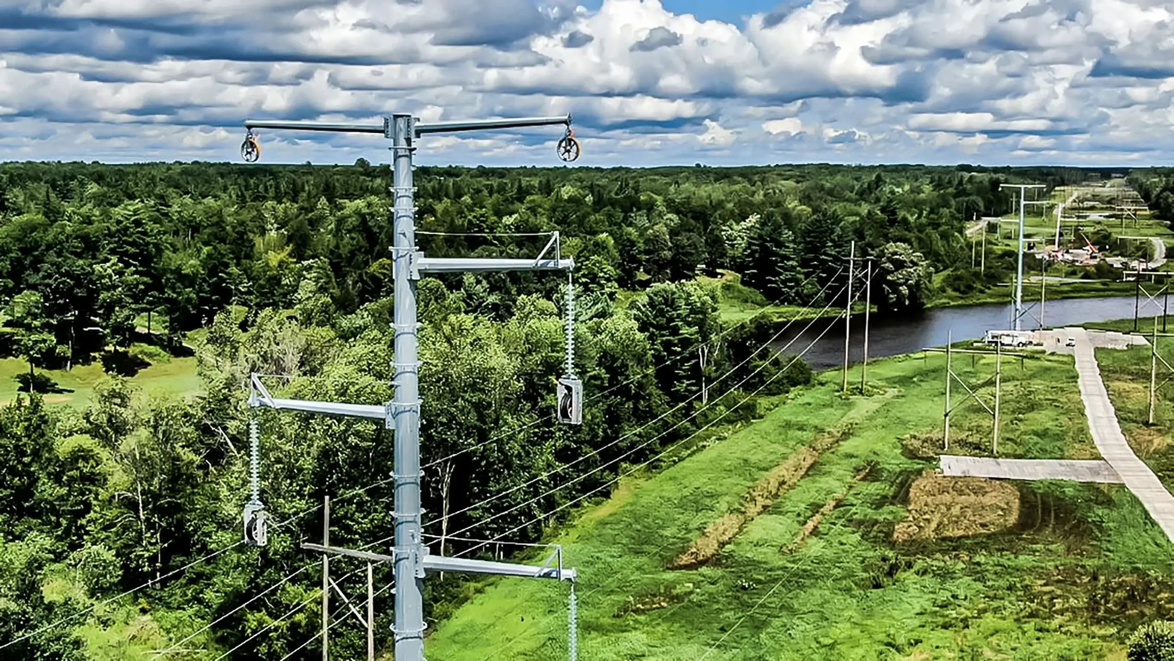 Large power lines run through a green wooded, rural area.