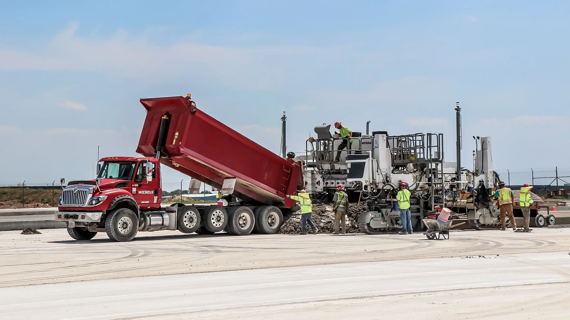 A dump truck assists a paving machine at an airport