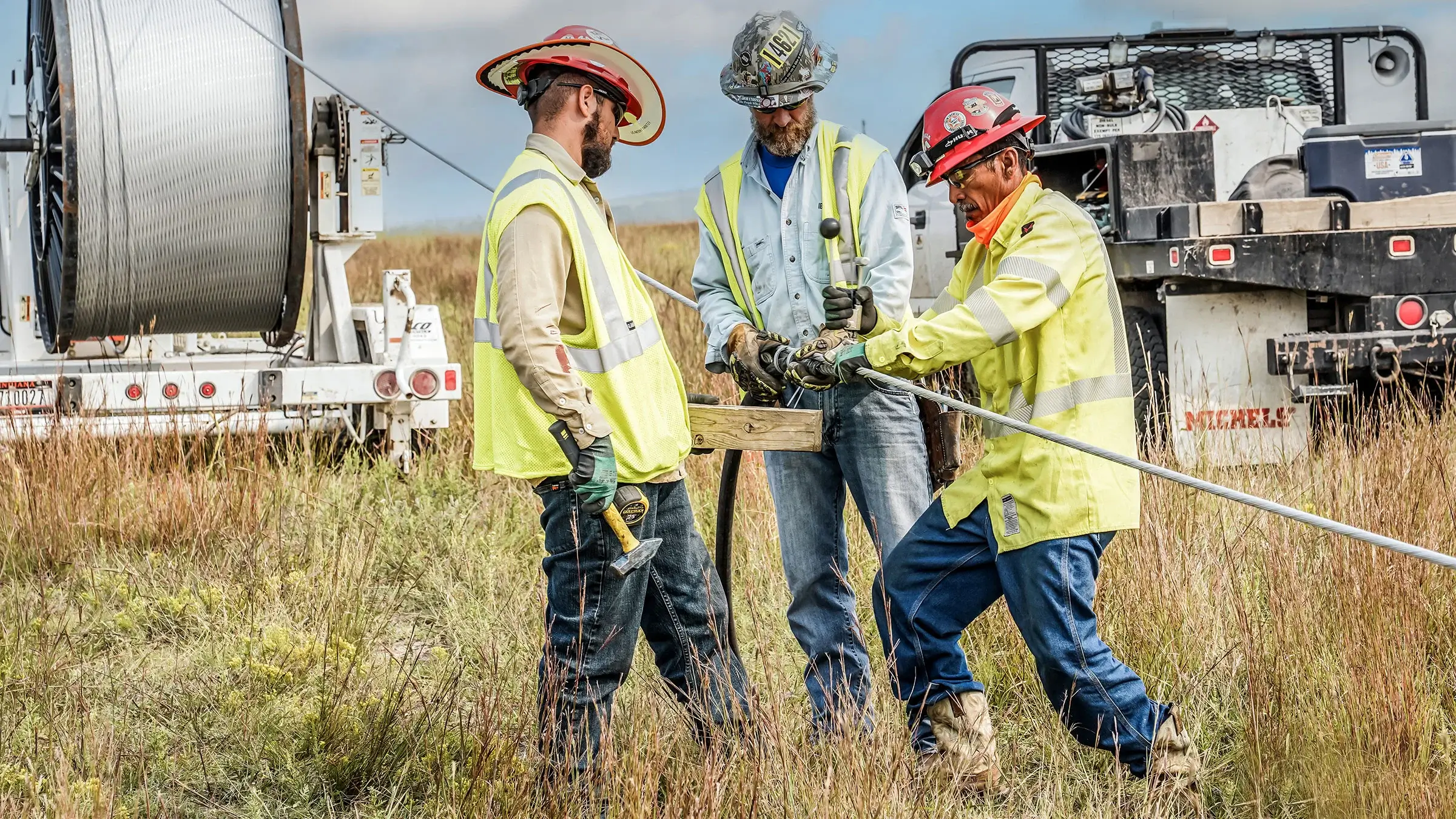 Three people prepare conductor to get pulled into place on a power line