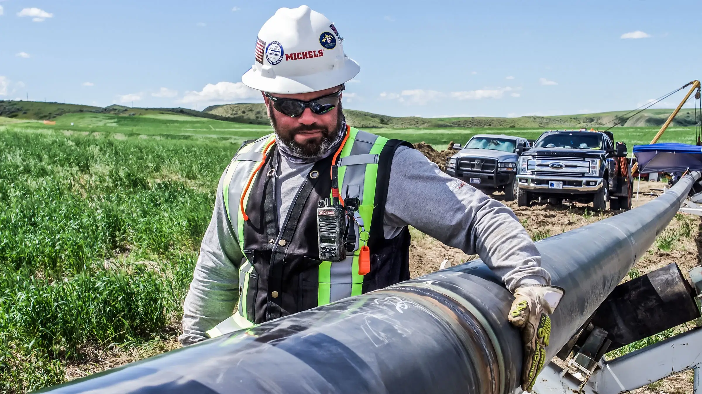 A Michels field worker inspects a pipeline in a large green field.