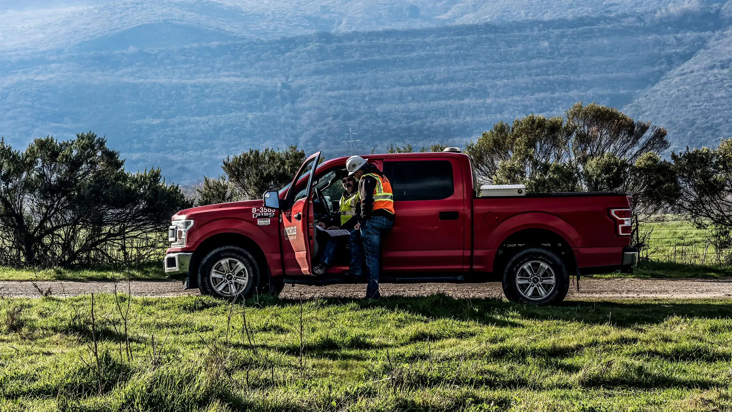 A project manager talks to a field work from inside a red pickup truck