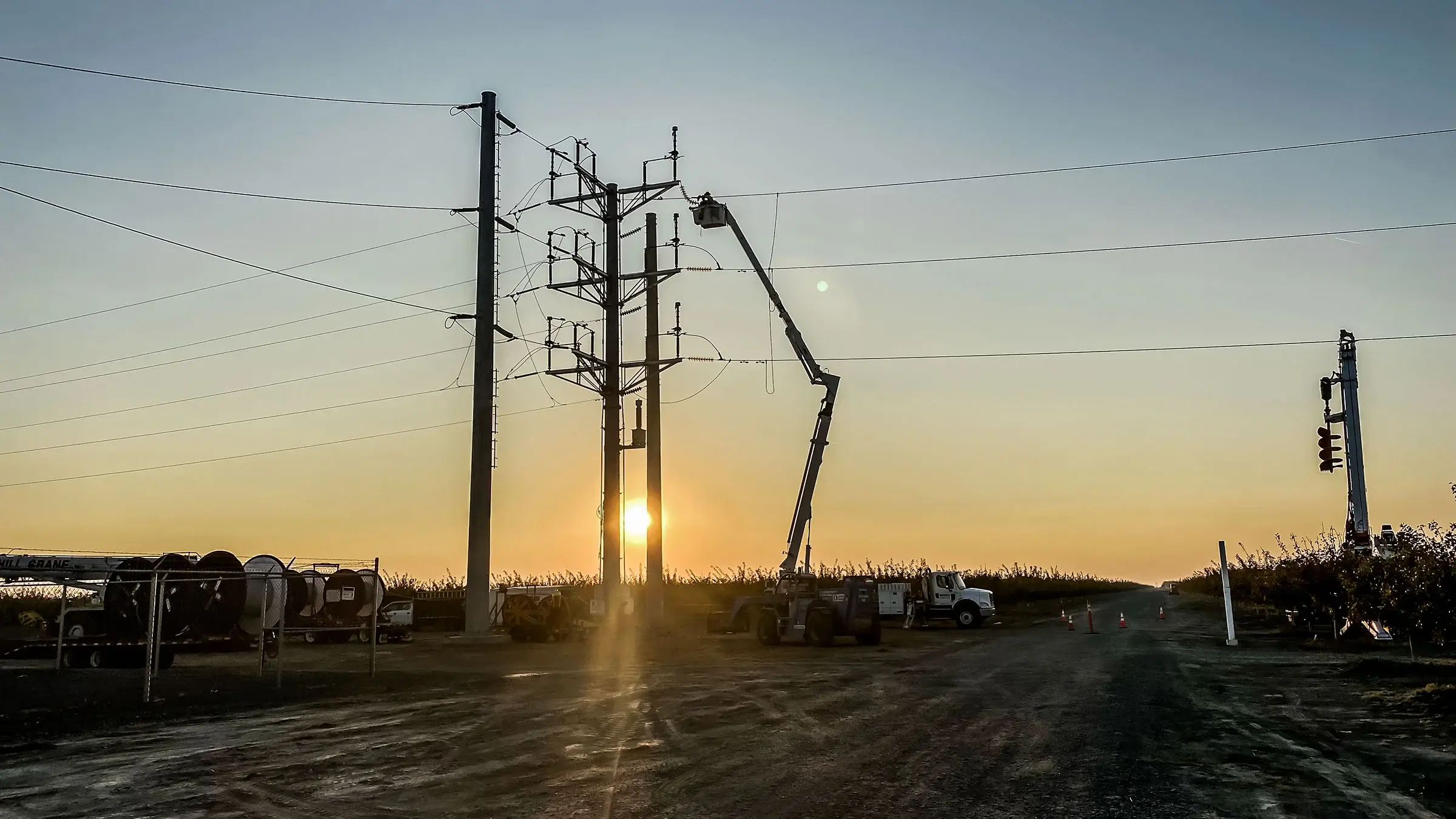 Bucket truck is extended to work on a power pole during golden hour.