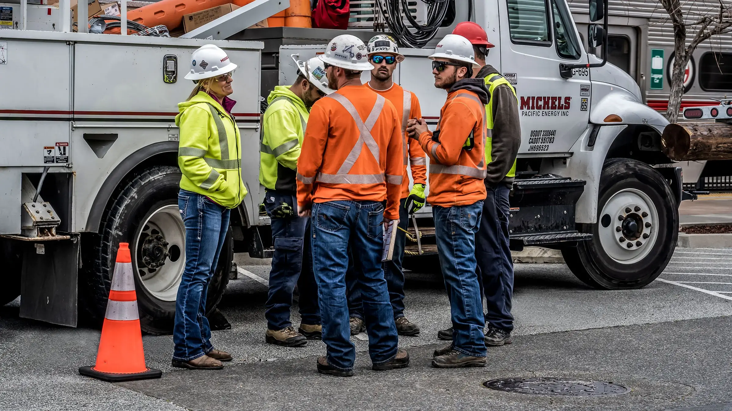 Group of workers wearing safety equipment standing in front of a bucket truck discussing a project.