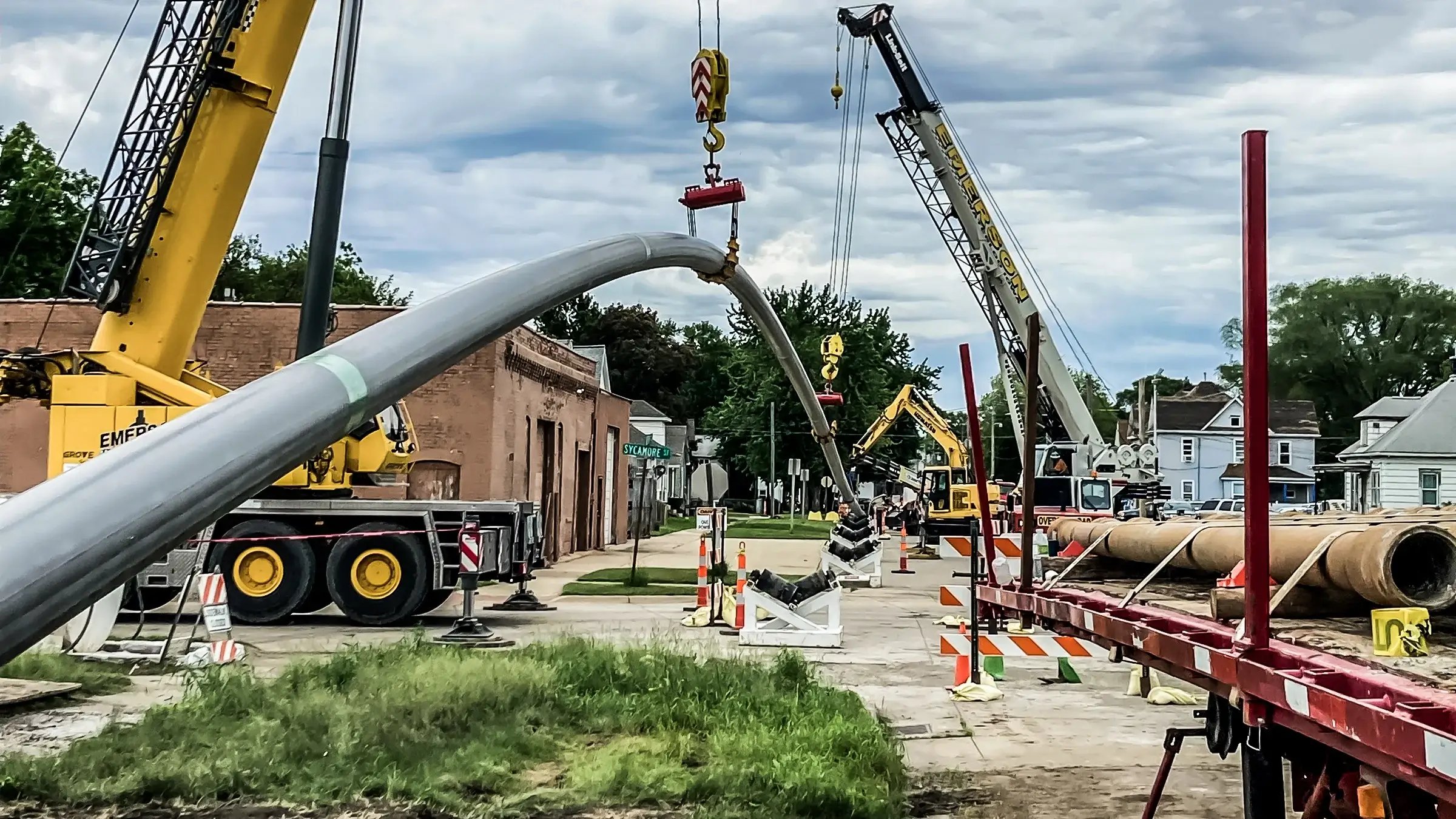 Several cranes assist in guiding pipeline into ground near residential homes