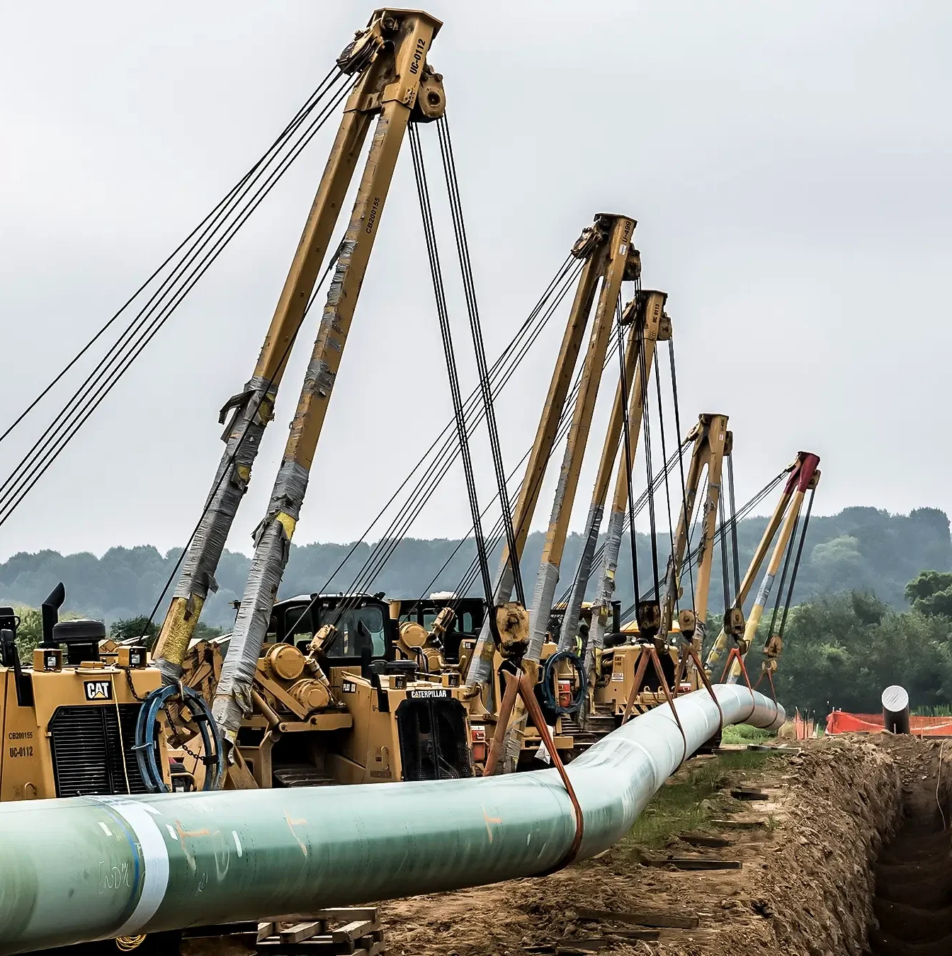 Pipelayers assist a large diameter pipeline into a trench.
