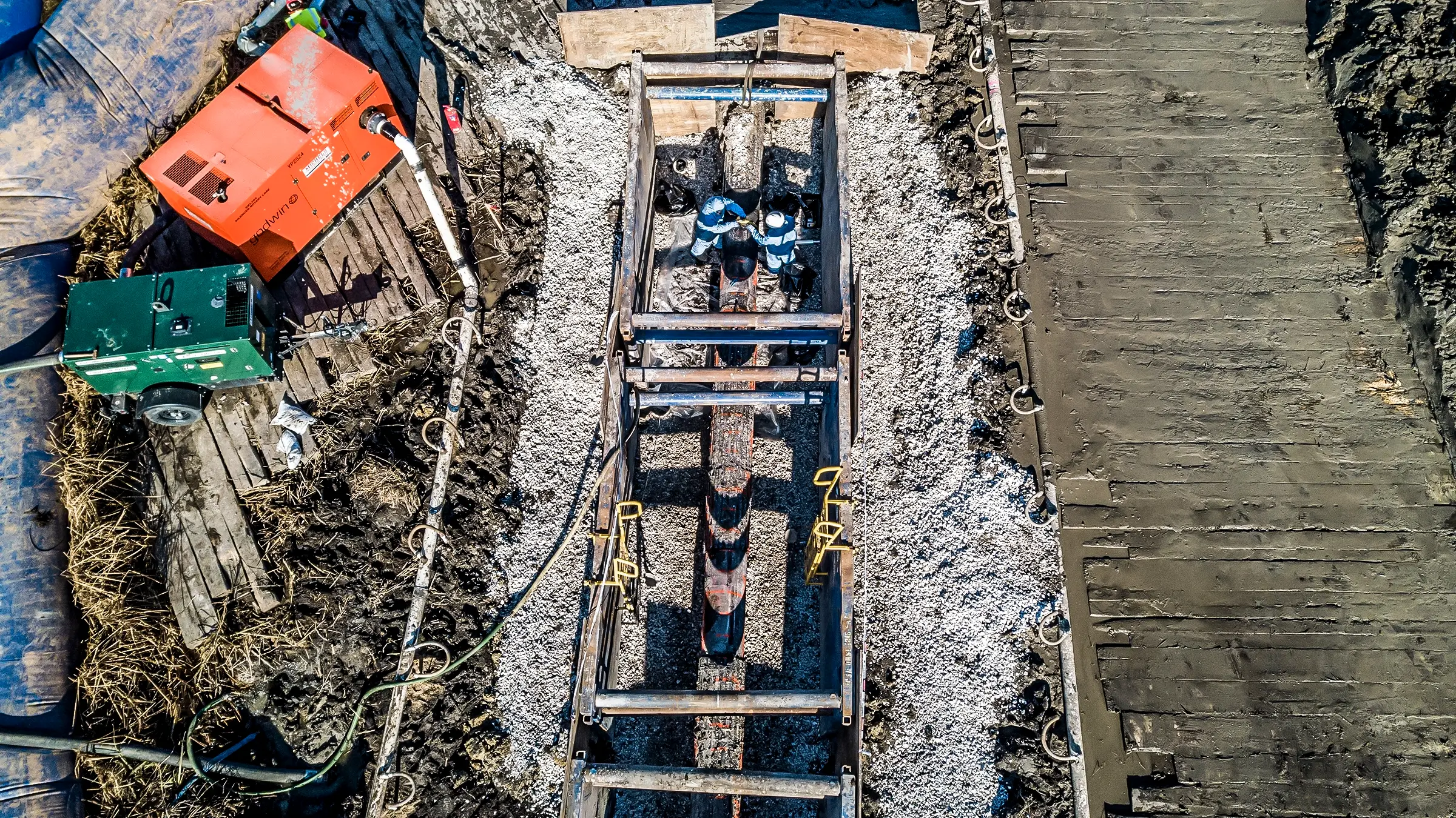 Two crew members work in a trench on a pipeline